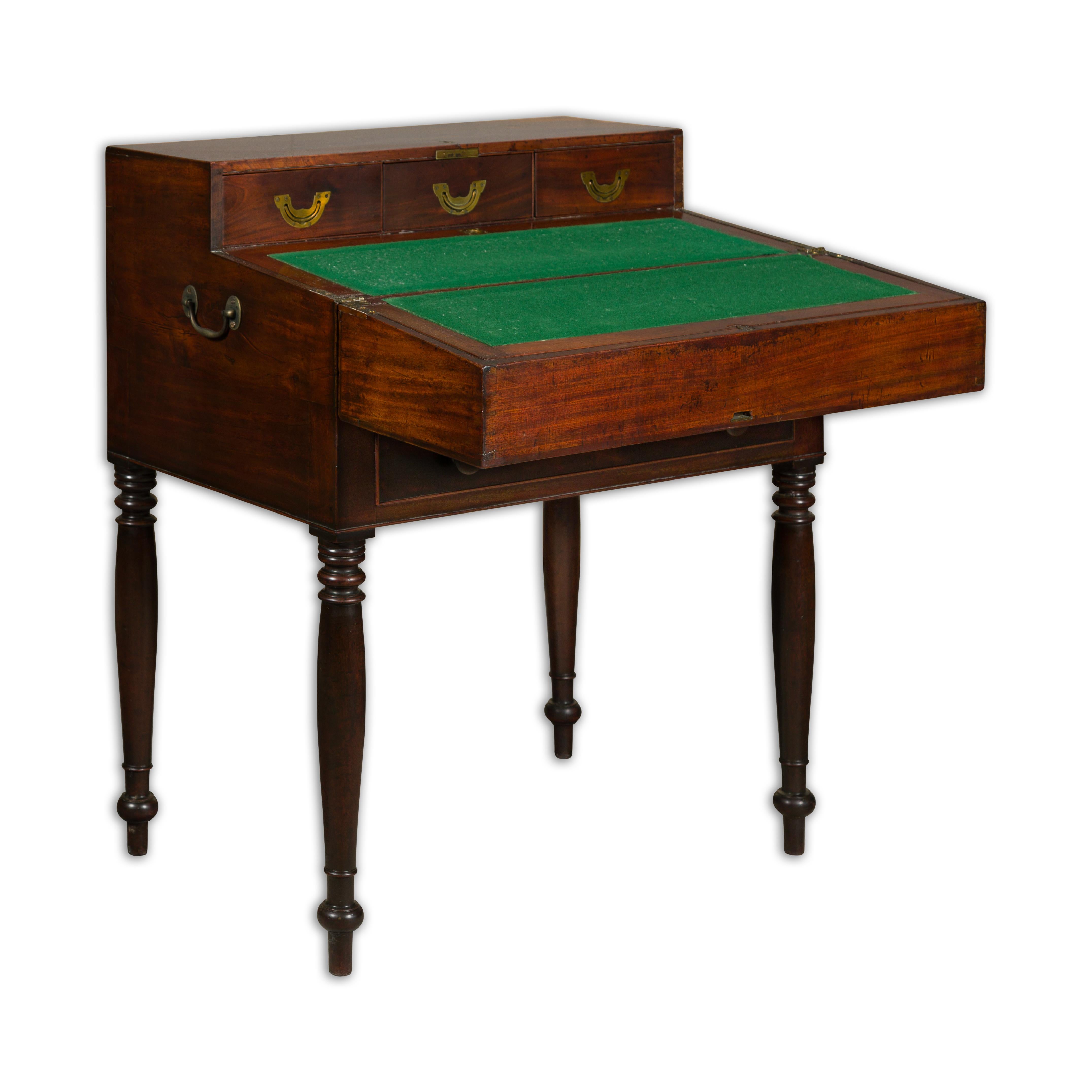 An English mahogany campaign period box on legs from the 19th century revealing a desk with drawers and green felt. This English mahogany campaign period box on legs from the 19th century is a captivating piece of functional artistry. Crafted with