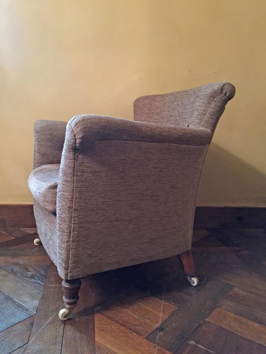 Elegant English late 19th-early 20th century Howard type upholstered club chair. Rolled and buttoned back and arms with a buttoned swell front and standing on turned mahogany legs with original brass and ceramic castors. This chair is as comfortable