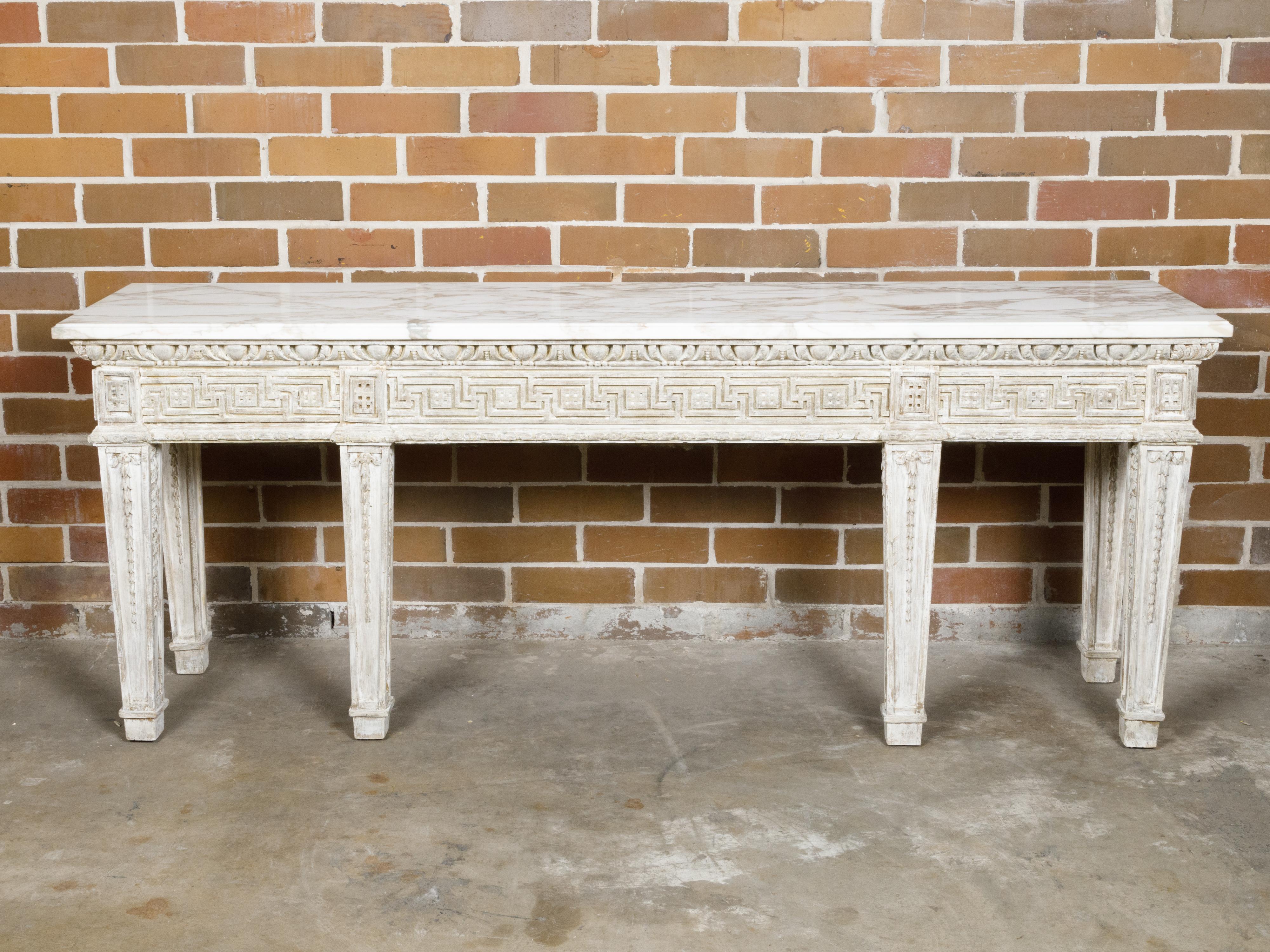 An English console table from the 19th century with white veined marble top, distressed off-white painted finish and carved Greek Key on the apron. This 19th-century English console table beautifully marries classic design with an air of distressed