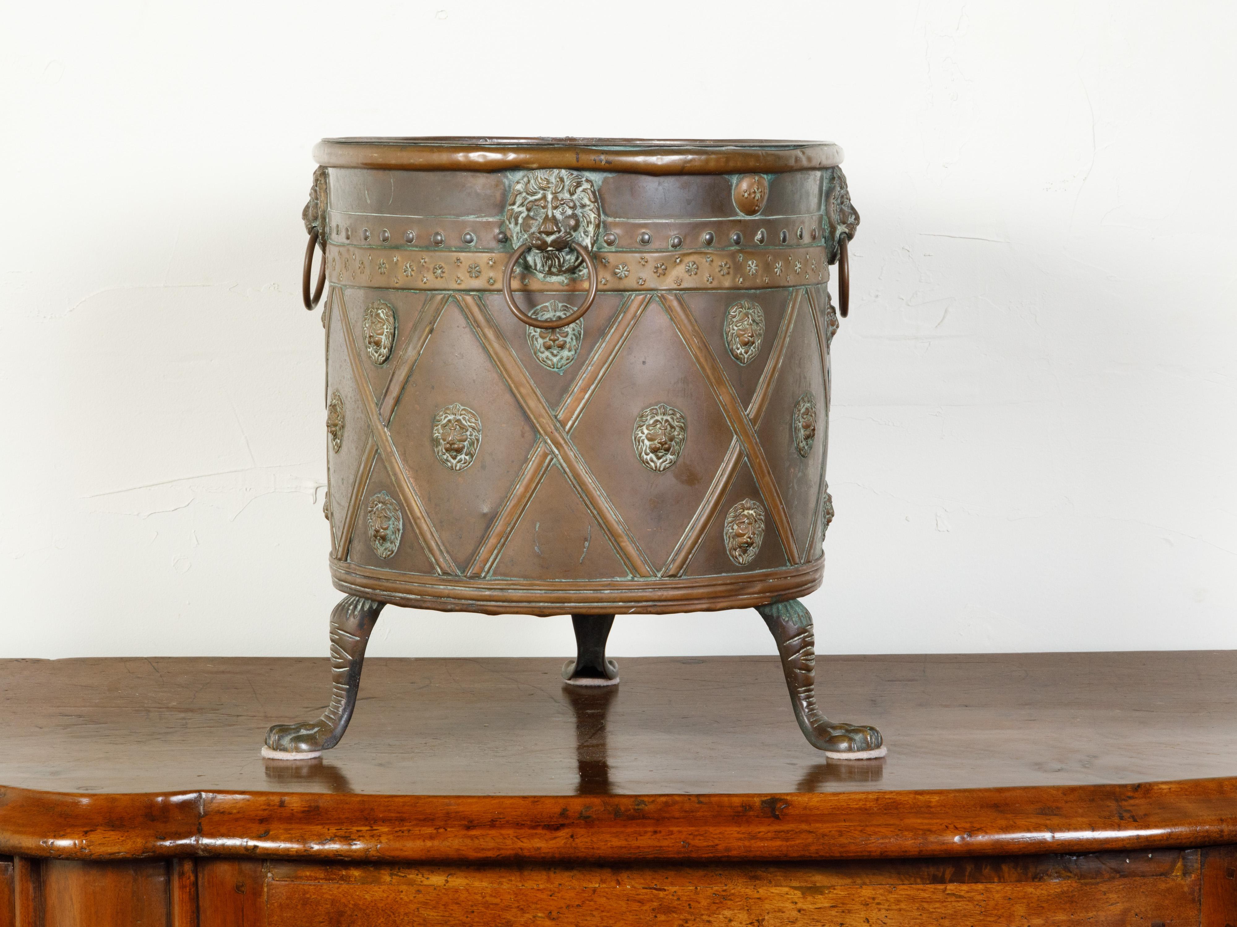 An English copper planter from the 19th century, with lion heads, diamond motifs and paw feet. Created in England during the 19th century, this copper planter features a circular body adorned with a rhythmic arrangement of lion heads, surrounded by