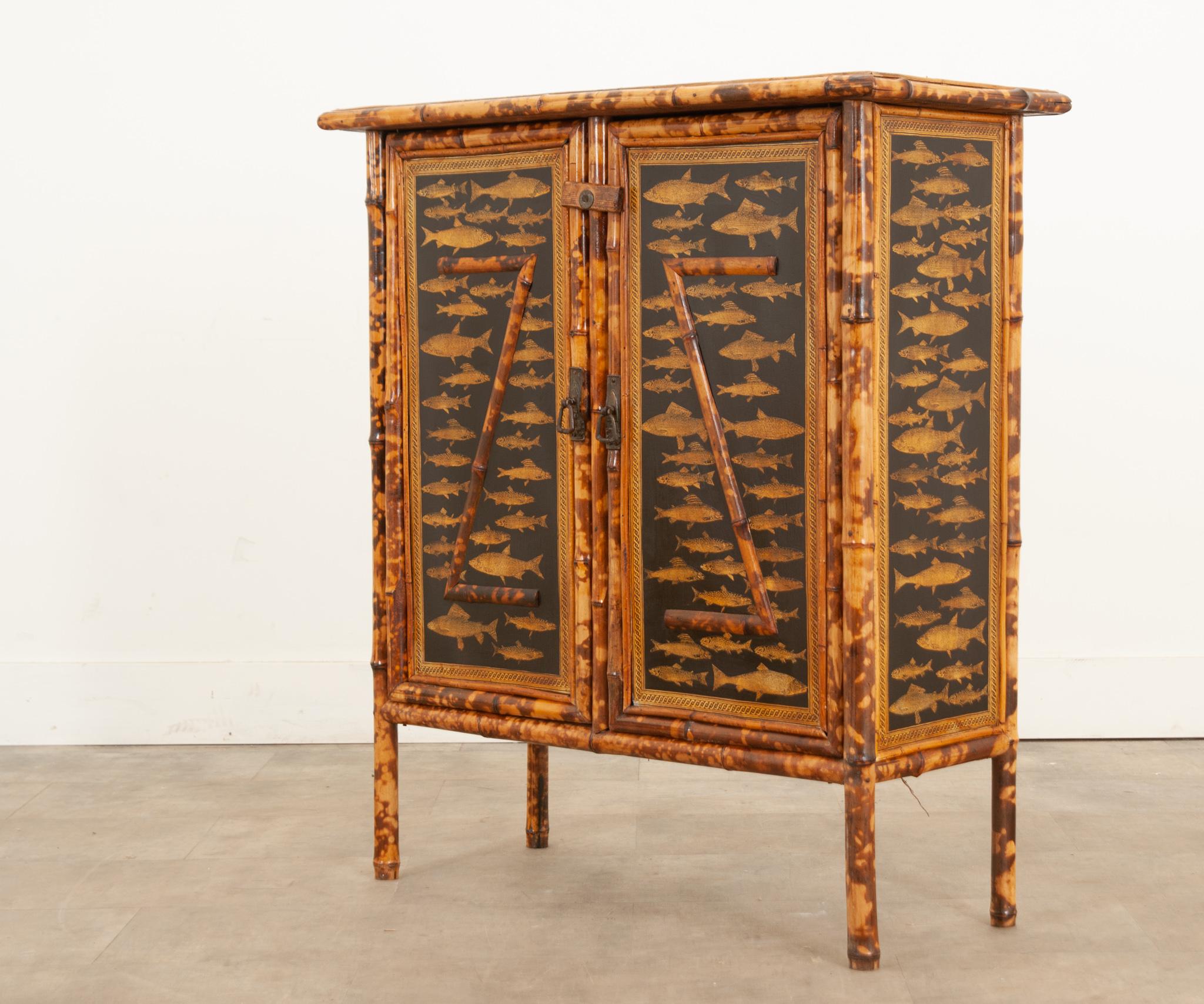 This delightful 19th century English bamboo cabinet has recently been decoupaged with a fish motif on the front, sides, and top. The door latches closed before an interior storage compartment outfitted with three spacious shelves. Make sure to view
