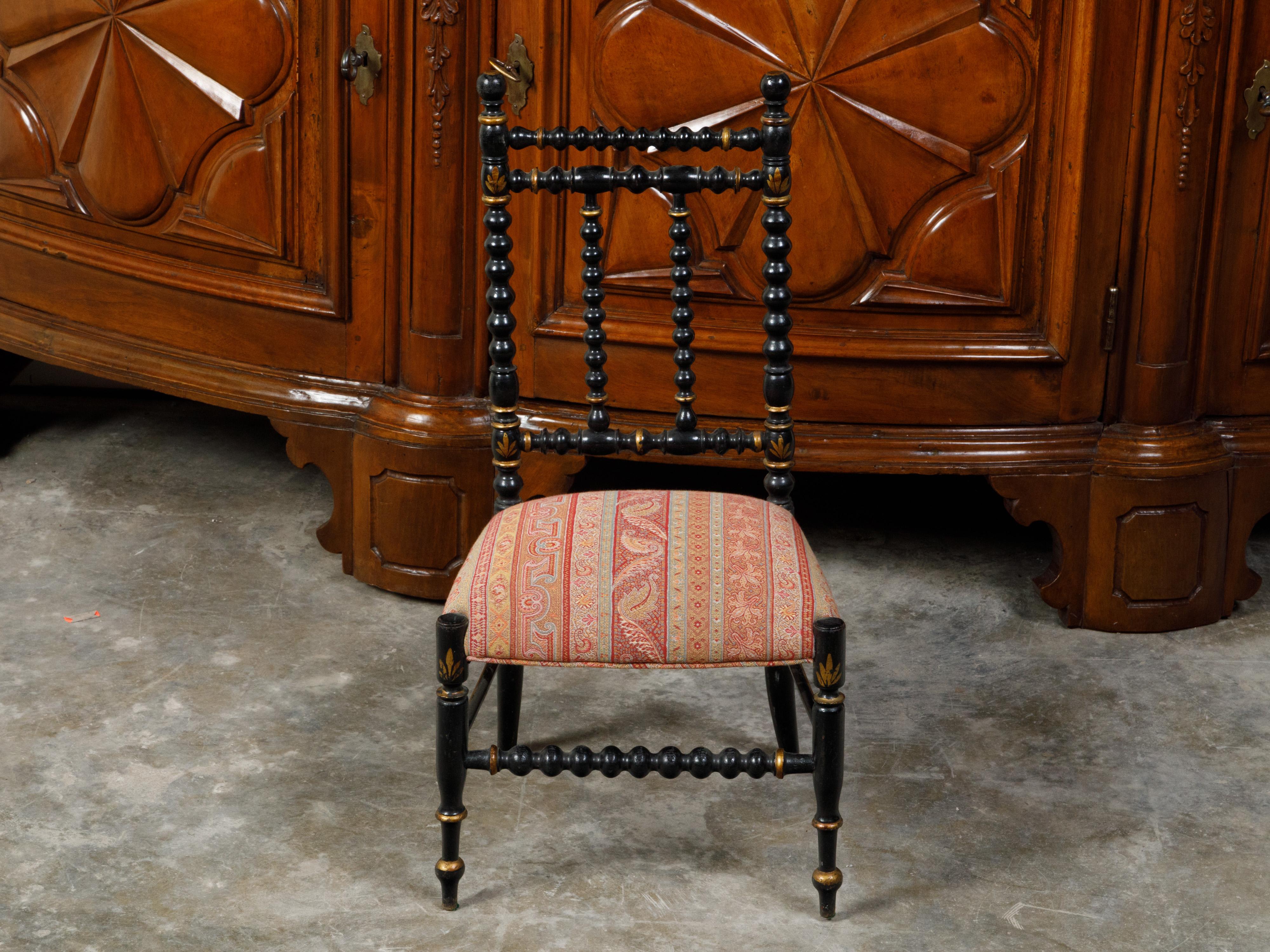 An English ebonized wood bobbin child's chair from the 19th century, with woven upholstery. Created in England during the 19th century, this wooden child's chair features an ebonized bobbin structure accented with gilt motifs. Showcasing a seat