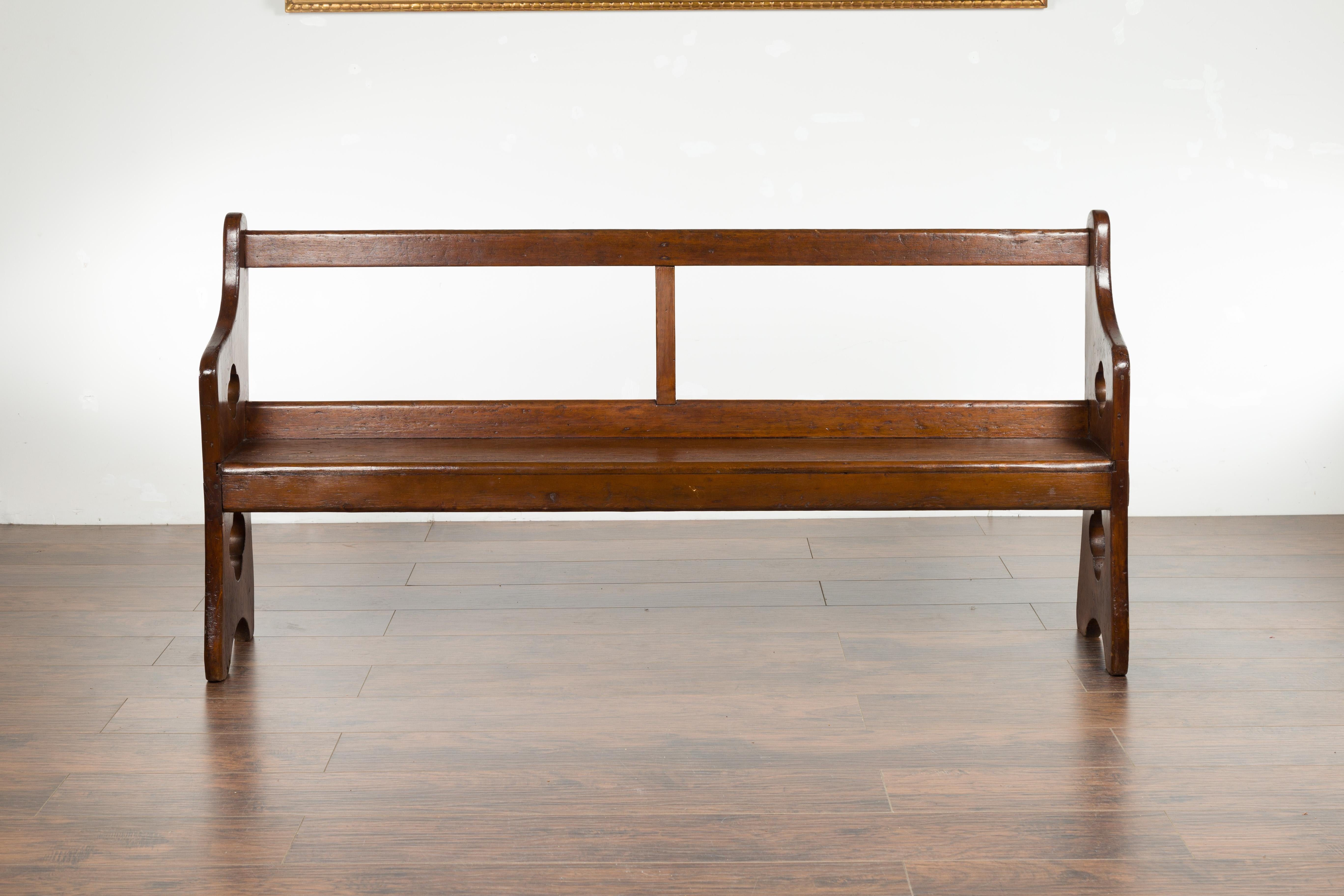 An English elm and oak bench from the 19th century, with pierced quatrefoil motifs and wooden seat. Created in England during the 19th century, this elm and oak bench charms us with its rustic presence and lovely patina. An open back is connected to