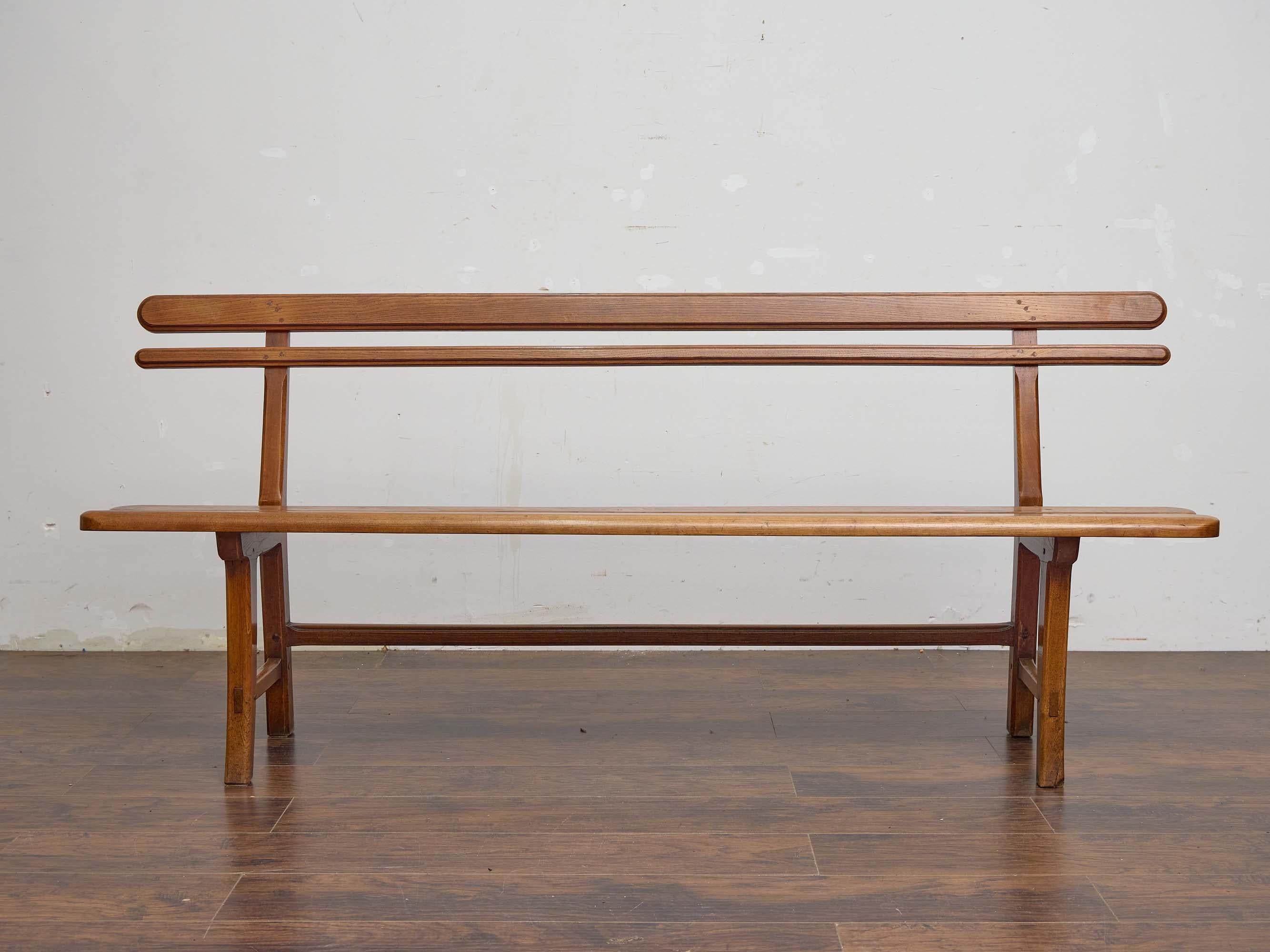 This 19th-century English bench is crafted from solid elm, showcasing the warm tone and fine grain for which the wood is prized. Spanning over six and a half feet in length, the design is simple yet well-proportioned, with a narrow double-slat