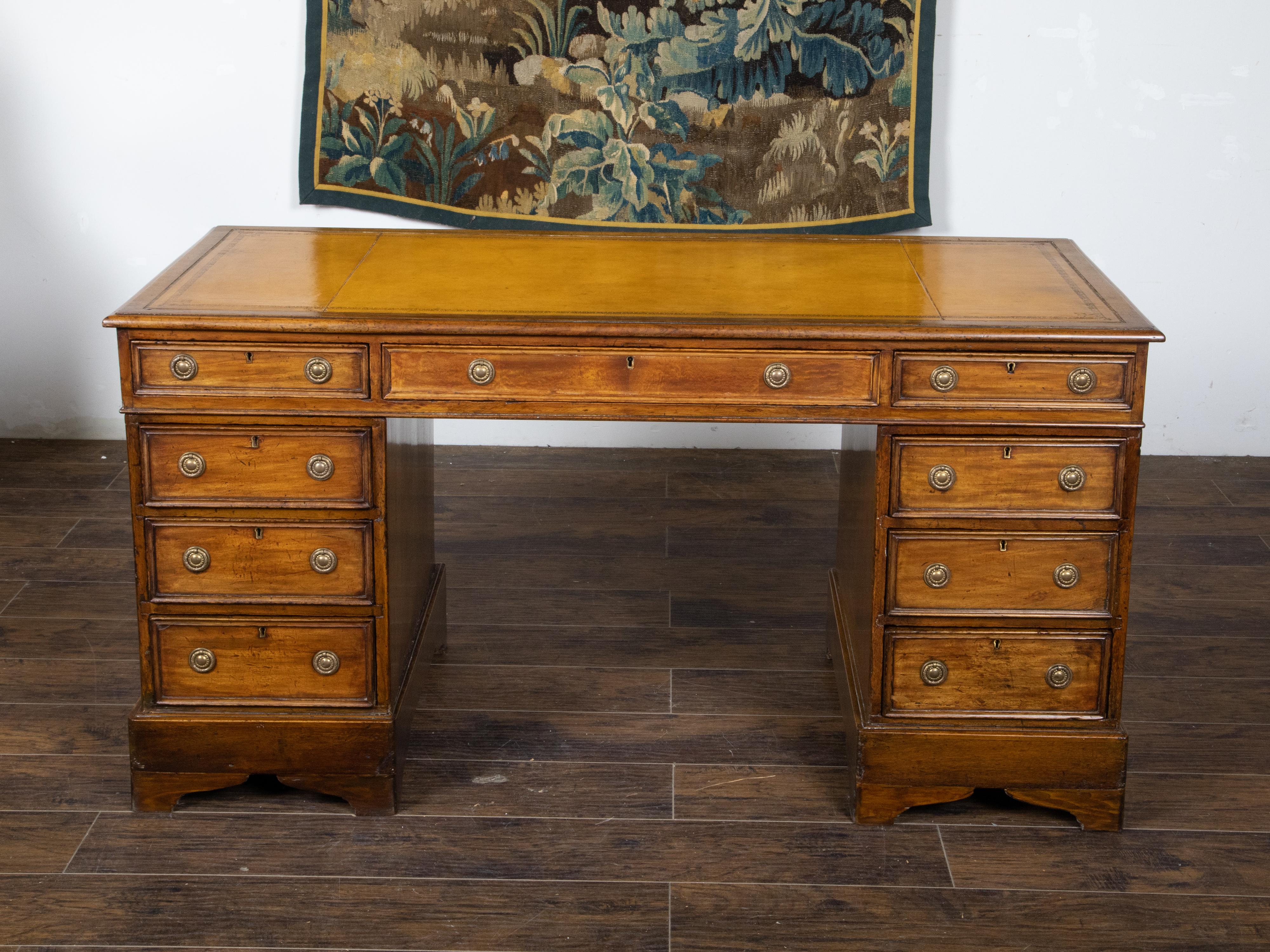 An English elm wood kneehole desk from the 19th century, with caramel leather top, tooled friezes, nine drawers and brass hardware. Created in England during the 19th century, this kneehole desk features a rectangular caramel colored partitioned