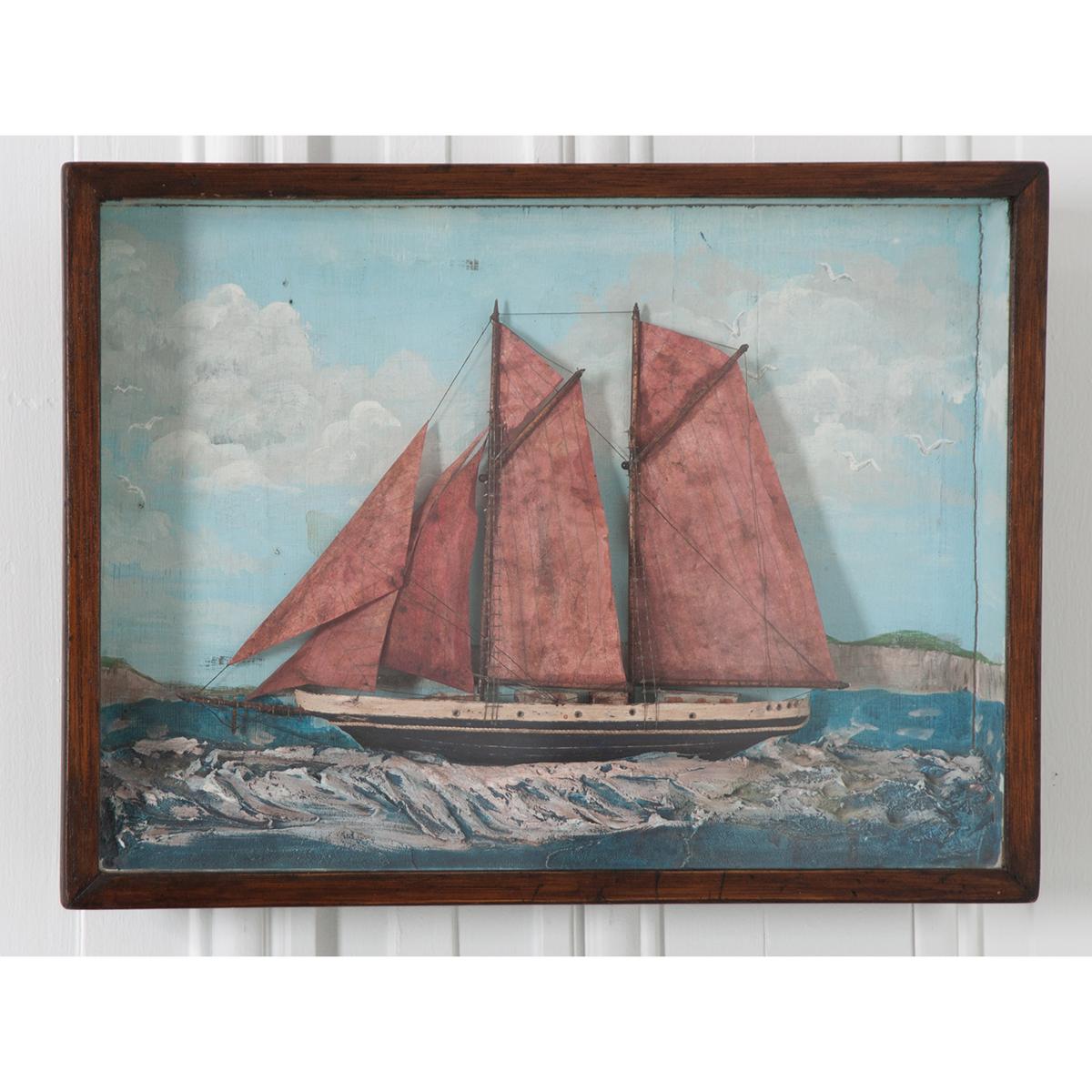 A brilliant English 19th century nautically themed diorama featuring a schooner with red sails. These three dimensional works of art were typically made by sailors in the 19th century.This diorama depicts a schooner at sea, but near the coast. Note