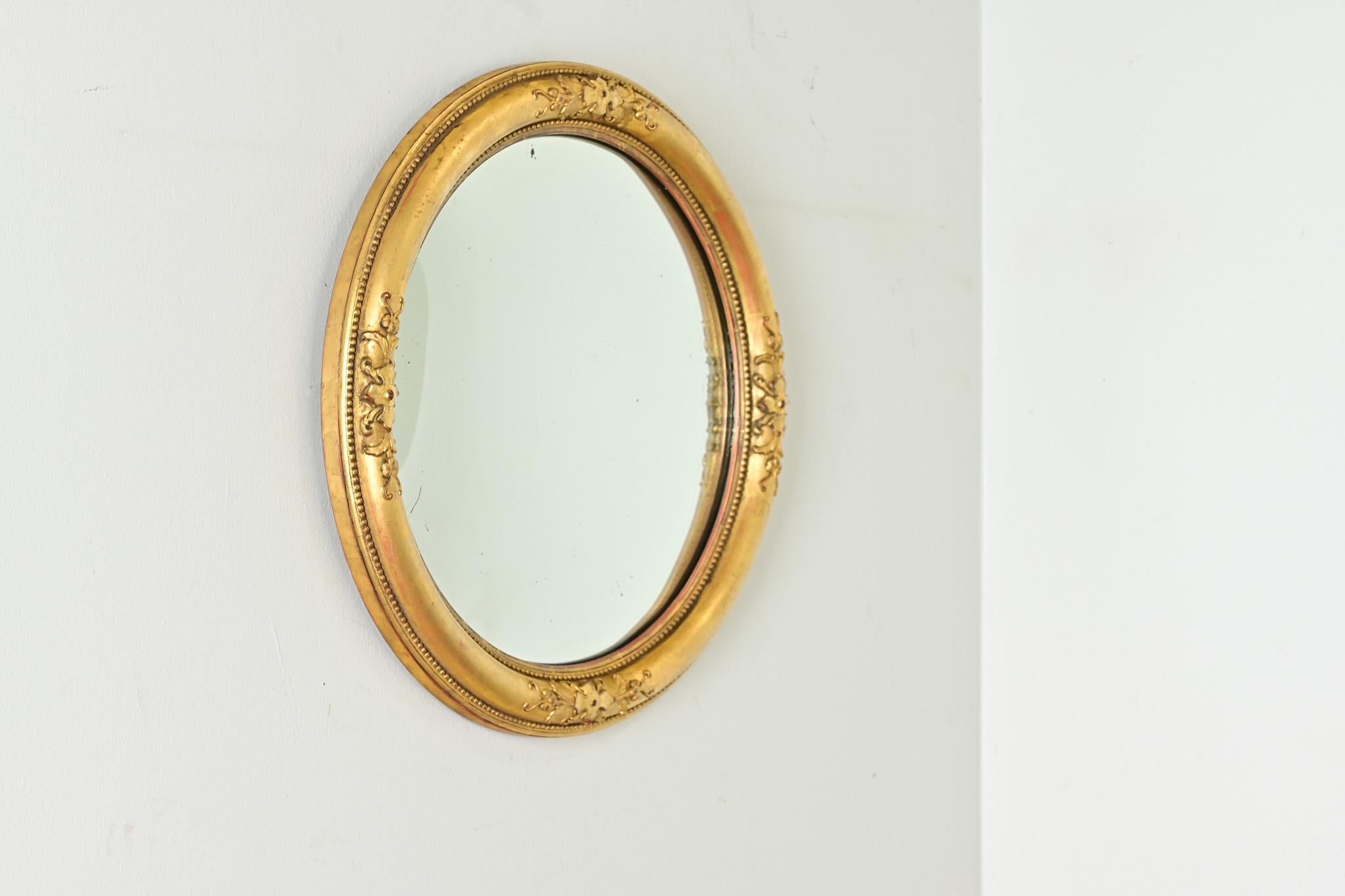 The elegance of this convex mirror is evident in the graceful carvings and velvety texture in the giltwork. Garnet-red bole accentuates the eye of the quatrefoil, stationed at the four cardinal points, while finely beaded molding creates definition.