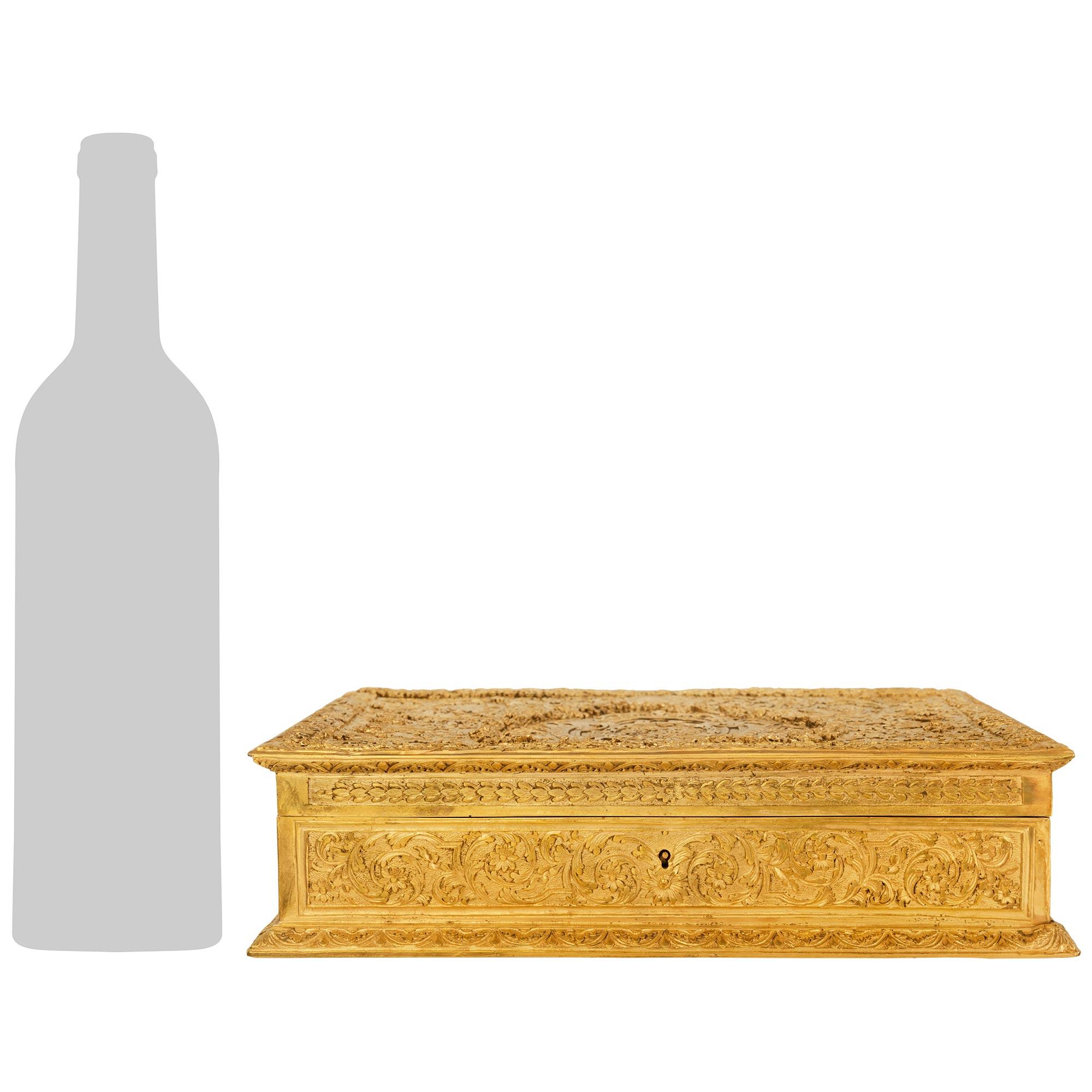 Excepcional caja inglesa del siglo XIX de metal dorado y terciopelo. Esta caja, maravillosamente decorativa, se eleva sobre una base plana decorada con guirnaldas de follaje ondulado que conducen al cuerpo, en el que se aprecian diseños de estilo