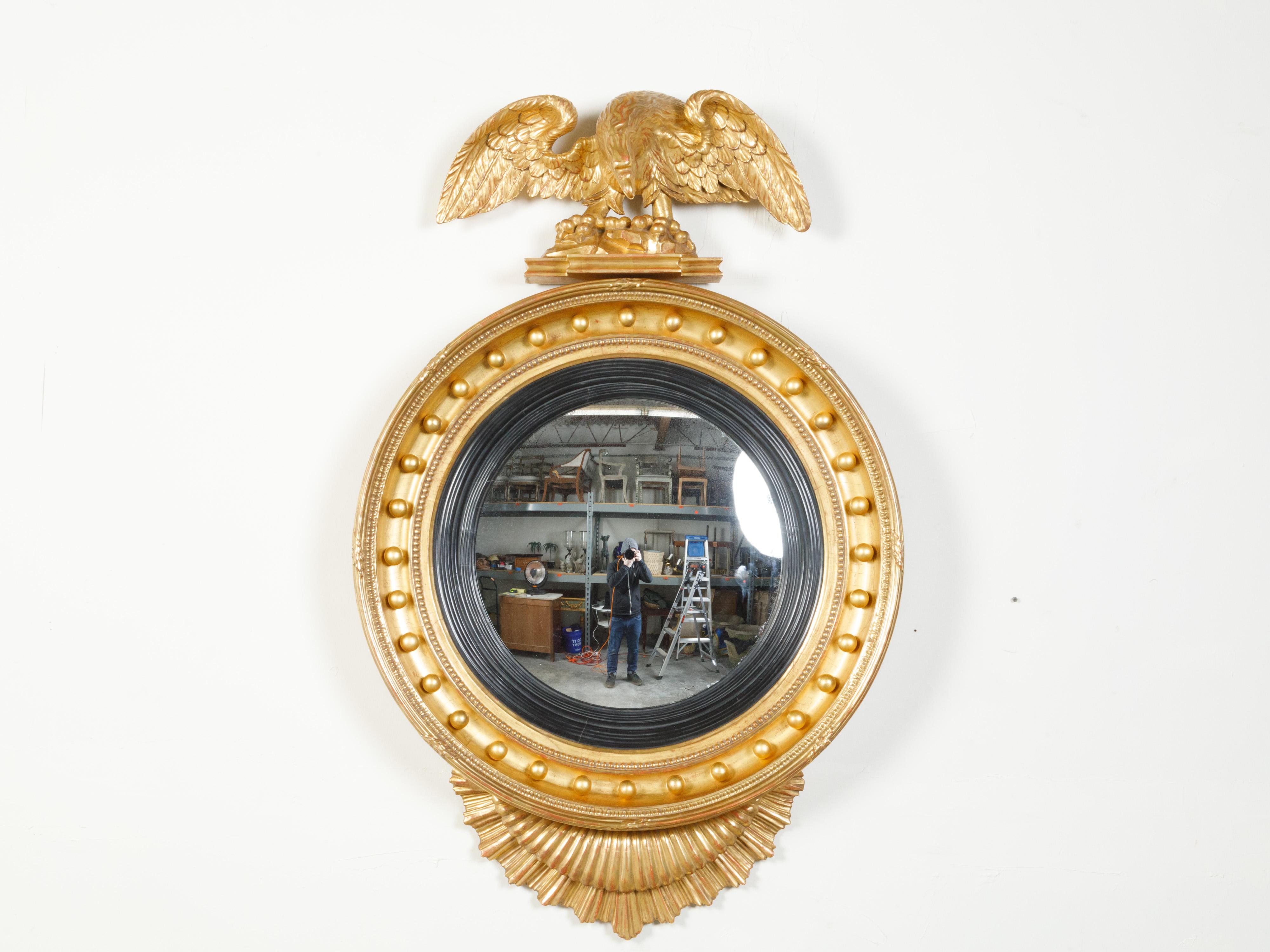 An English giltwood convex girandole bullseye mirror from the 19th century, with carved eagle motif. Created in England during the 19th century, this giltwood girandole mirror attracts our attention with its eagle marking the upper section. His