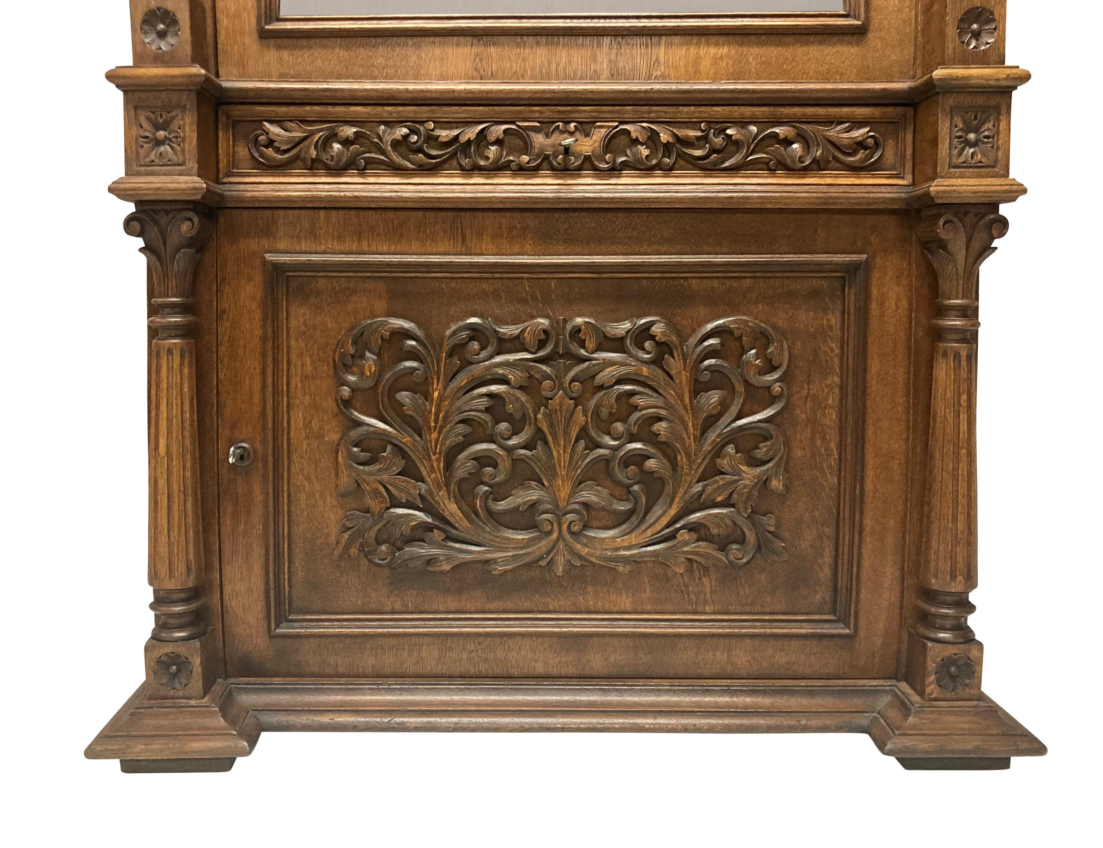 A large English solid oak gun cabinet in the Romanesque manner, with a glazed (clear glass) lockable upper cabinet for eight guns, with a lockable drawer beneath and lower cupboard. Decorated throughout and with a good patina.