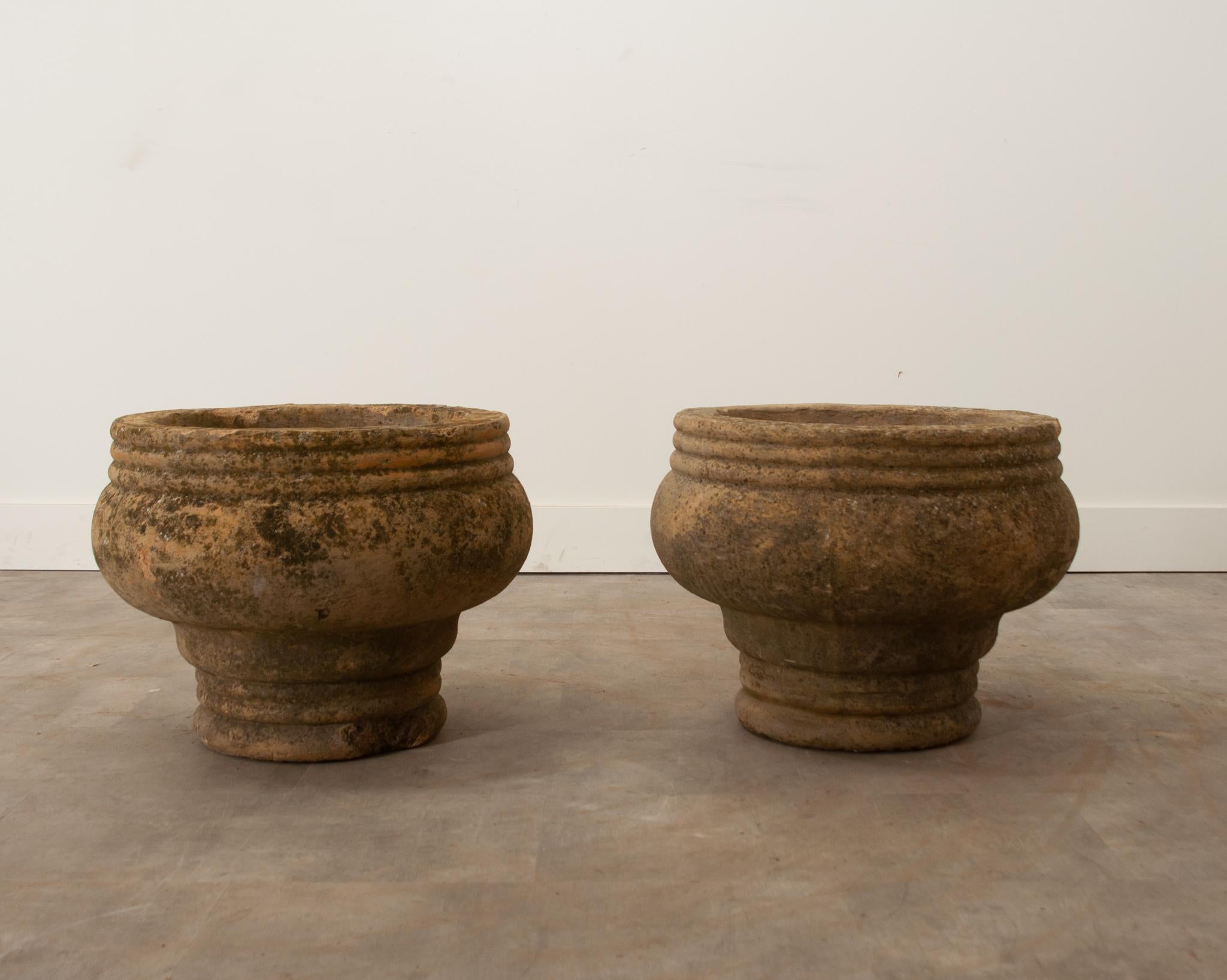 A handsome pair of heavy terracotta planters from 19th century England. Decades of weather exposure have given them a fascinating patina and variation in color. Holes for avoiding water collection are present. The interior measures 16” diameter and