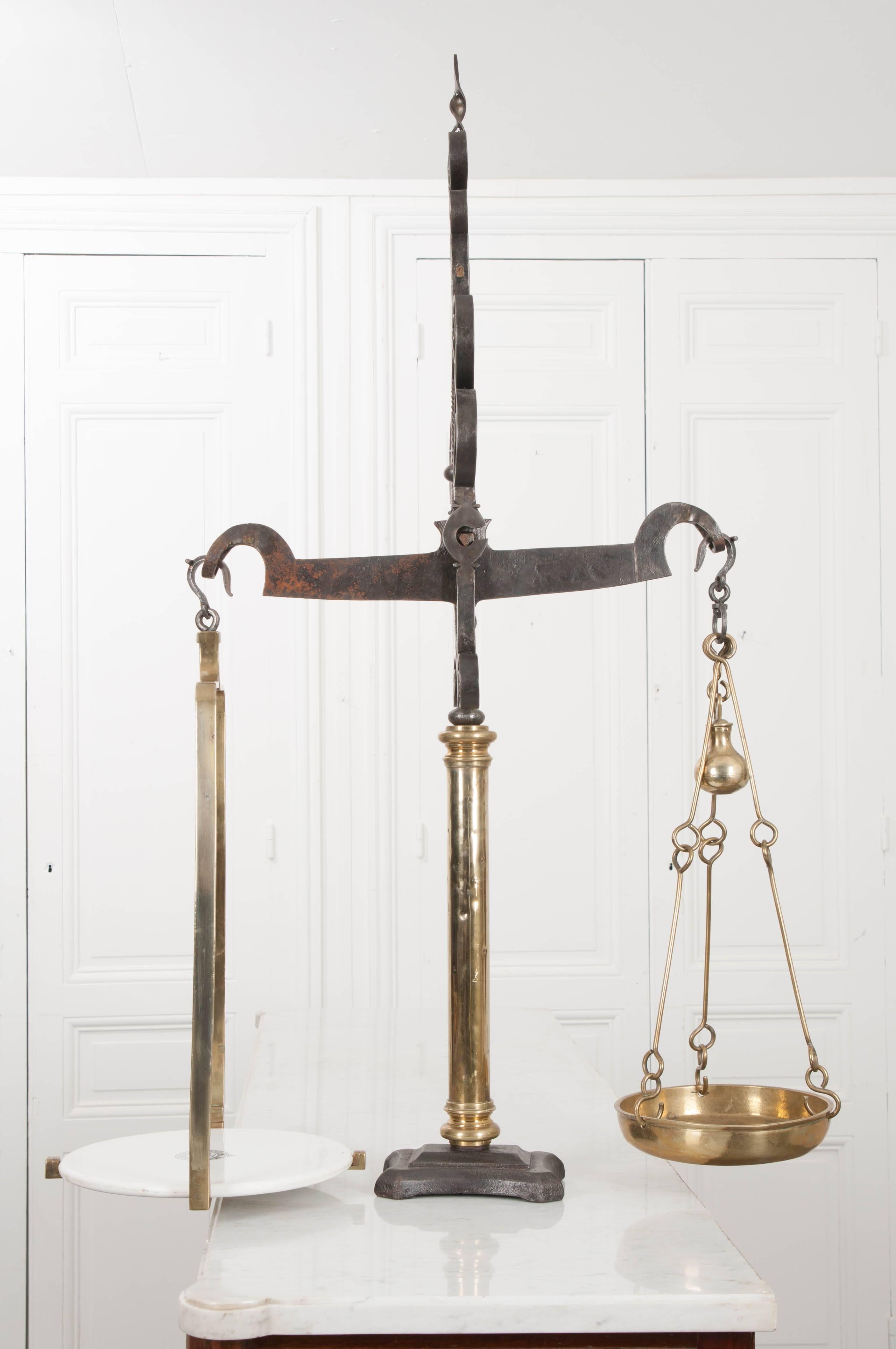 A grand Victorian-era balance scale, made in England by S. Banfield, circa 1855. This immense and ornately stylized “weighing machine” is a sight to see. Scrolled iron details create a finial above the top beam that incorporates the antique’s