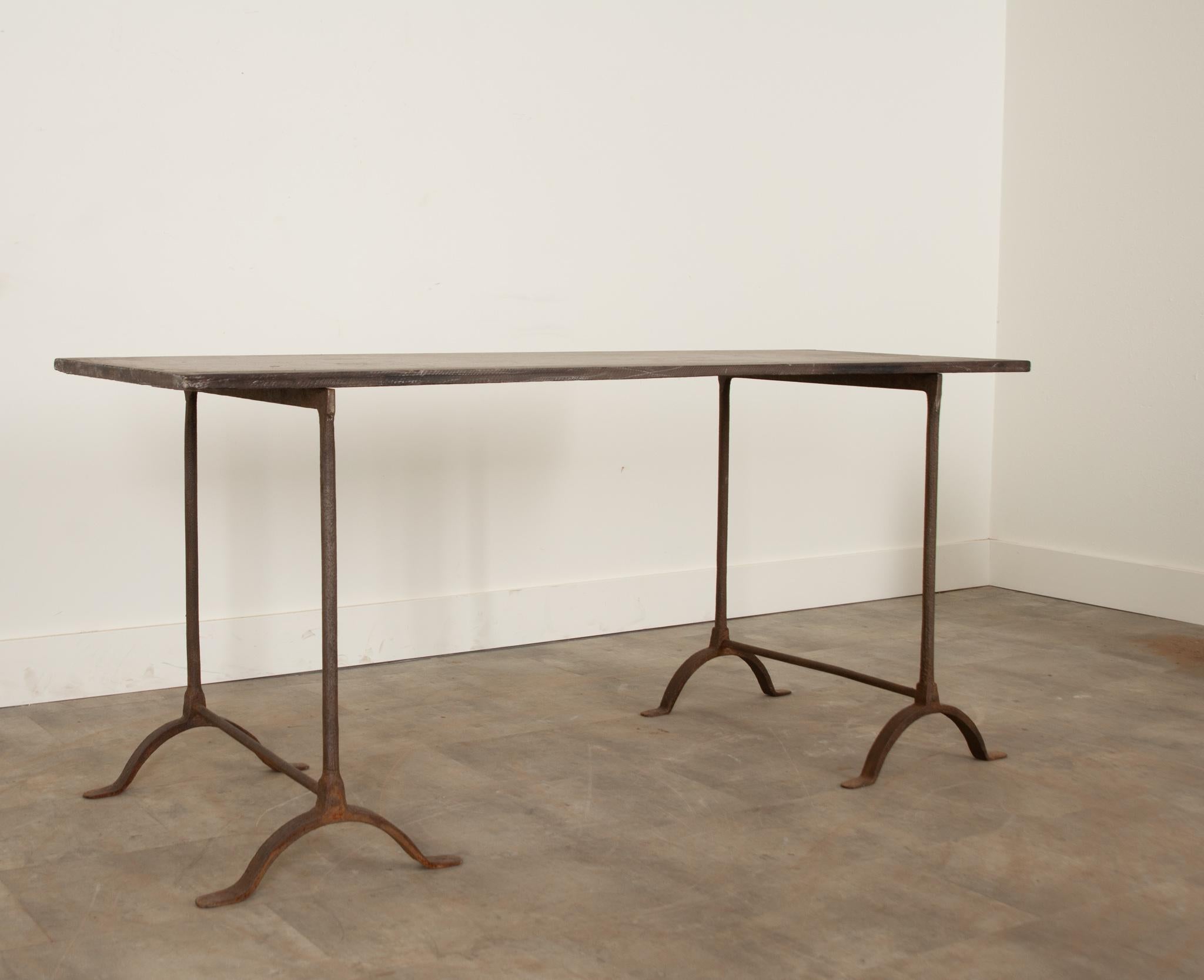 Hand forged iron trestle table base with a natural finish, topped with a large single piece of patinated slate. The design of this table is very versatile. The table comes in three pieces; the piece of slate and two iron legs. Easy to move and