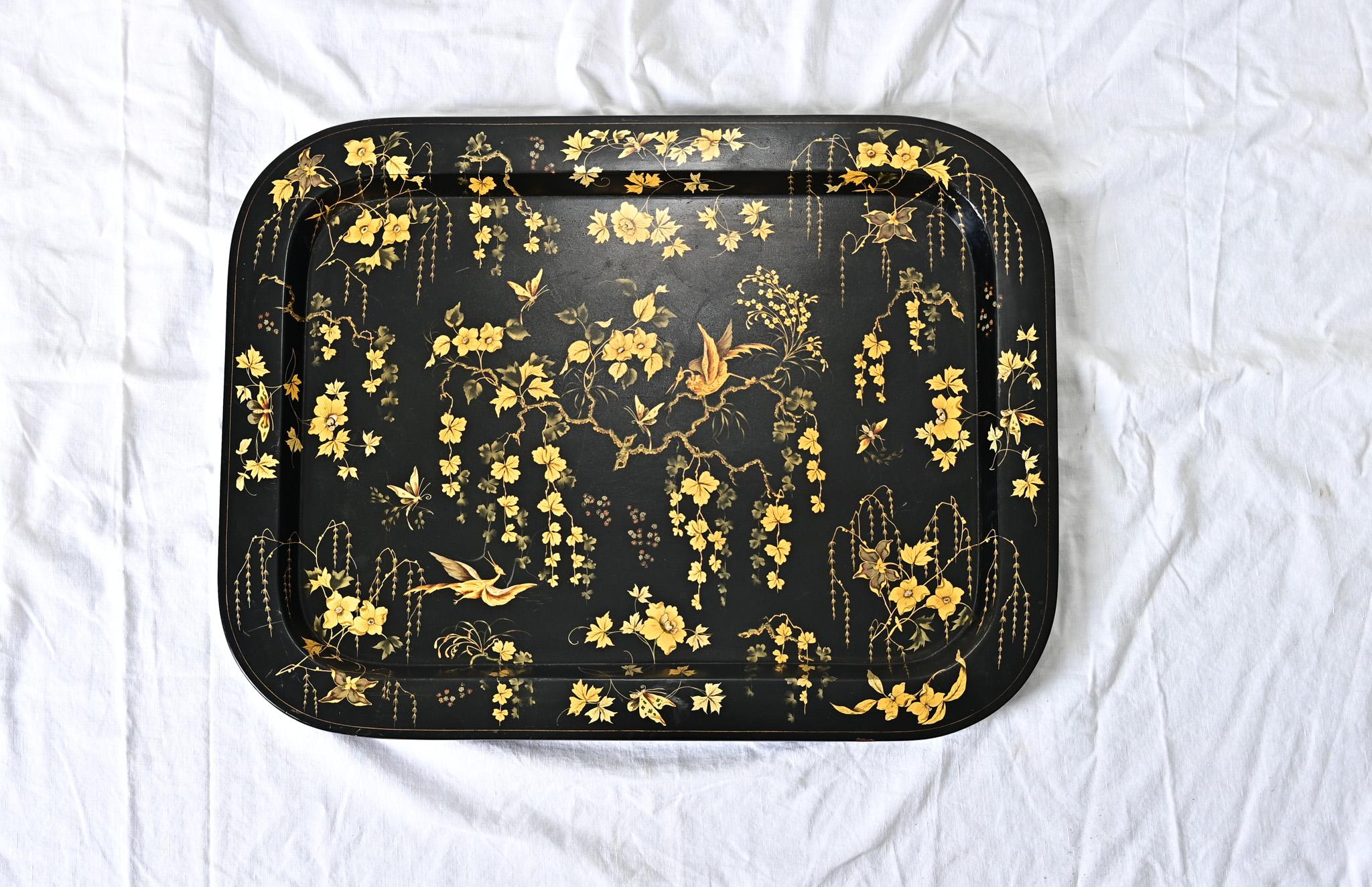 A stunning papier mache tray from England, 19th century, with “Japanned” black lacquer and parcel gilt illustrations covering the surface. The tray is glowing from the intricate depictions of stylized cranes, willow trees, and other flowering vines