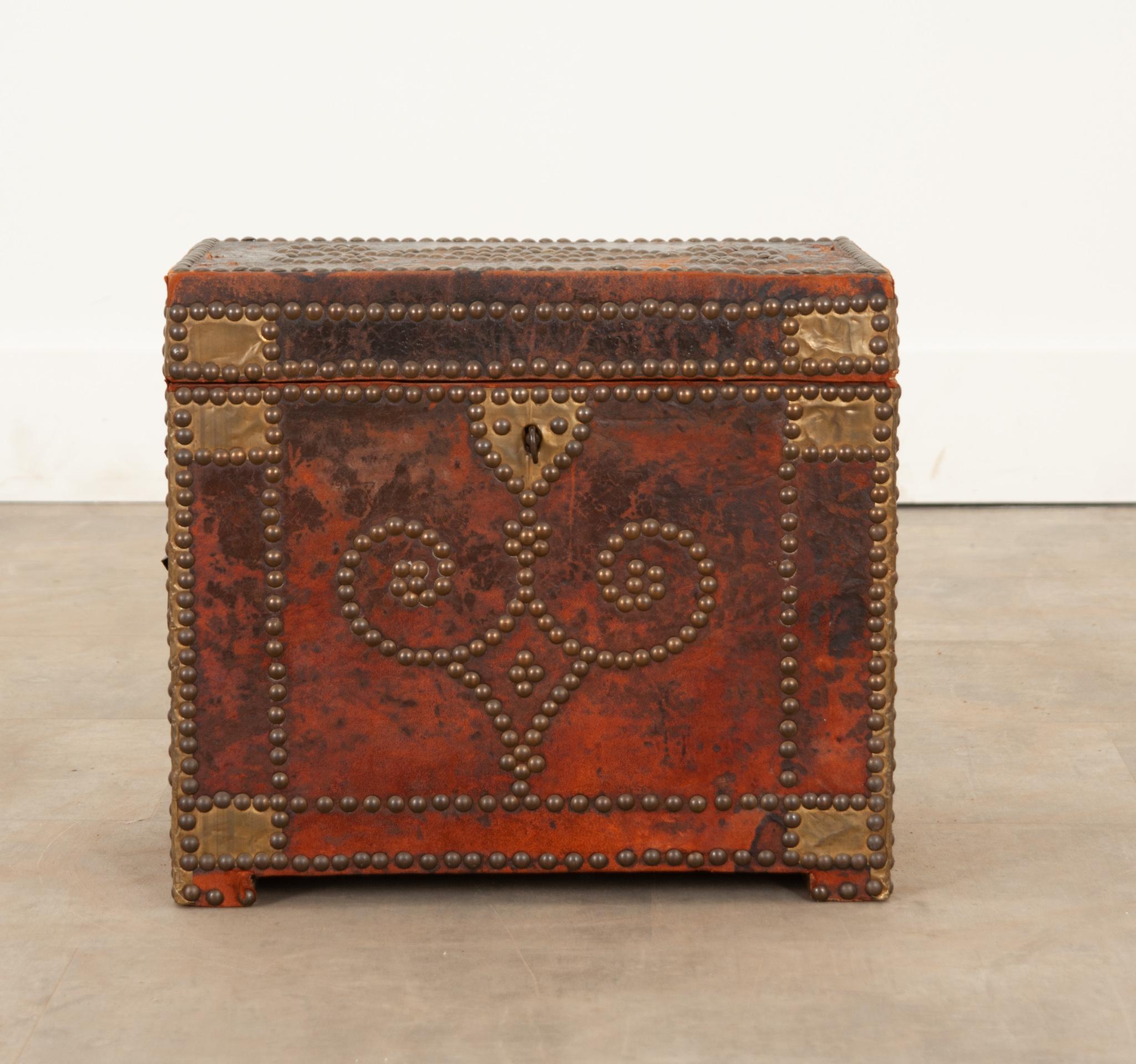 We absolutely love this decorative trunk from England! Bound in perfectly worn dark leather and adorned with brass studs in swirling patterns. The lock is in working condition and includes one key. A pair of simple handles on each side make it easy