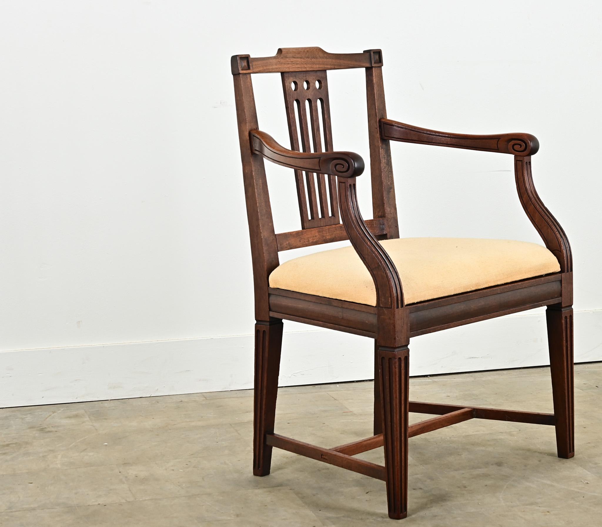 An English carved mahogany armchair from the 1800’s. This comfortable and stylish single armchair is perfect for an occasional chair or at a desk. The geometric carvings on the chair back compliment the sloping chair arms and fluted, squared off