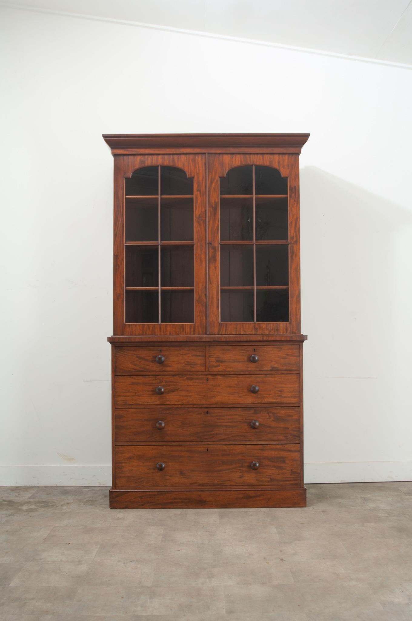 A rare English mahogany chest of drawers with a bookcase top. This cabinet has two glass front doors that open with a working lock and key to three adjustable interior shelves, 15”D. The chest has 5 working drawers all with easy to use turned knobs.