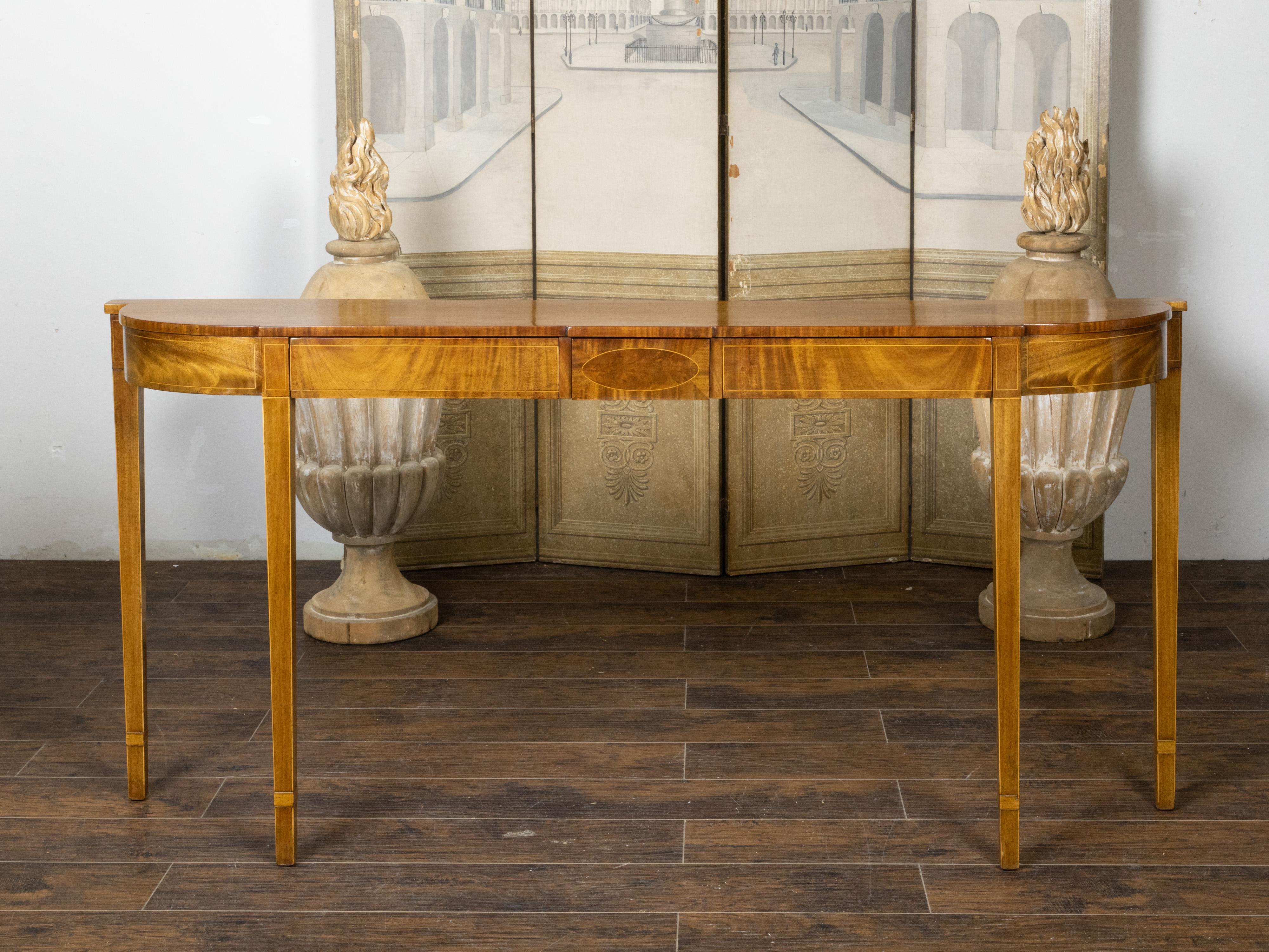 A long English Neoclassical style mahogany bow front console table from the 19th century, with three drawers, banding and tapered legs. Created in England during the 19th century, this Neoclassical style mahogany console table features a shaped top