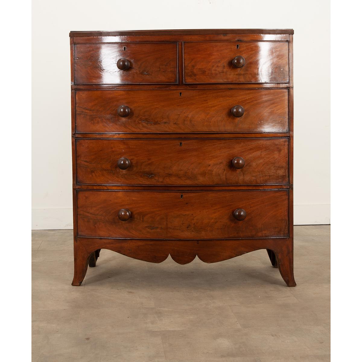 A gorgeous 19th century English mahogany chest of drawers with a bow front. It has a wonderful patina from years of loving care and use. The top sits over 5 drawers each fitted with simple brass escutcheon plates. No keys are present but smooth