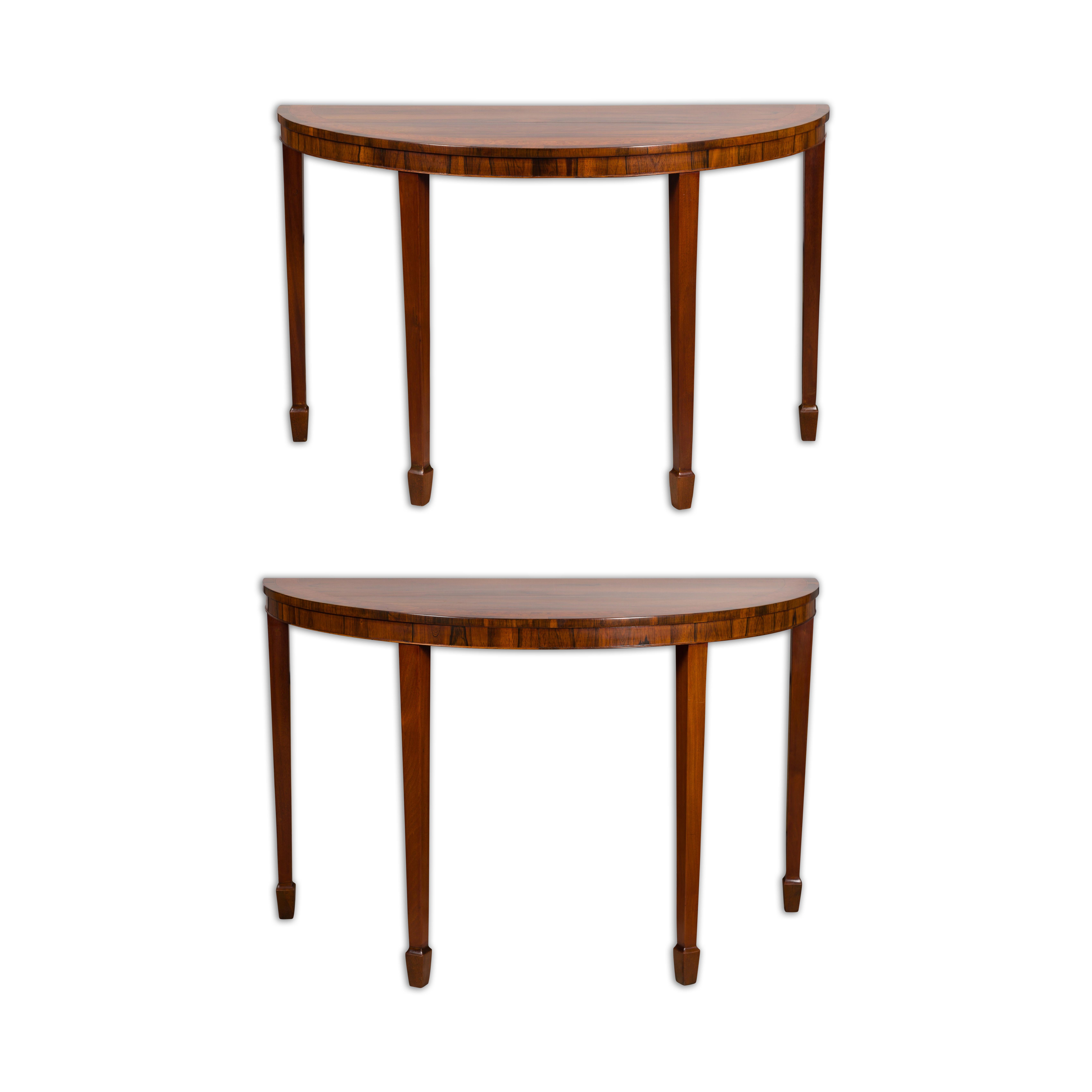 A pair of English mahogany demilune console tables from the 19th century with tapered legs, spade feet and thin banding. This pair of 19th-century English mahogany demilune console tables is a striking embodiment of classic elegance. Crafted with an