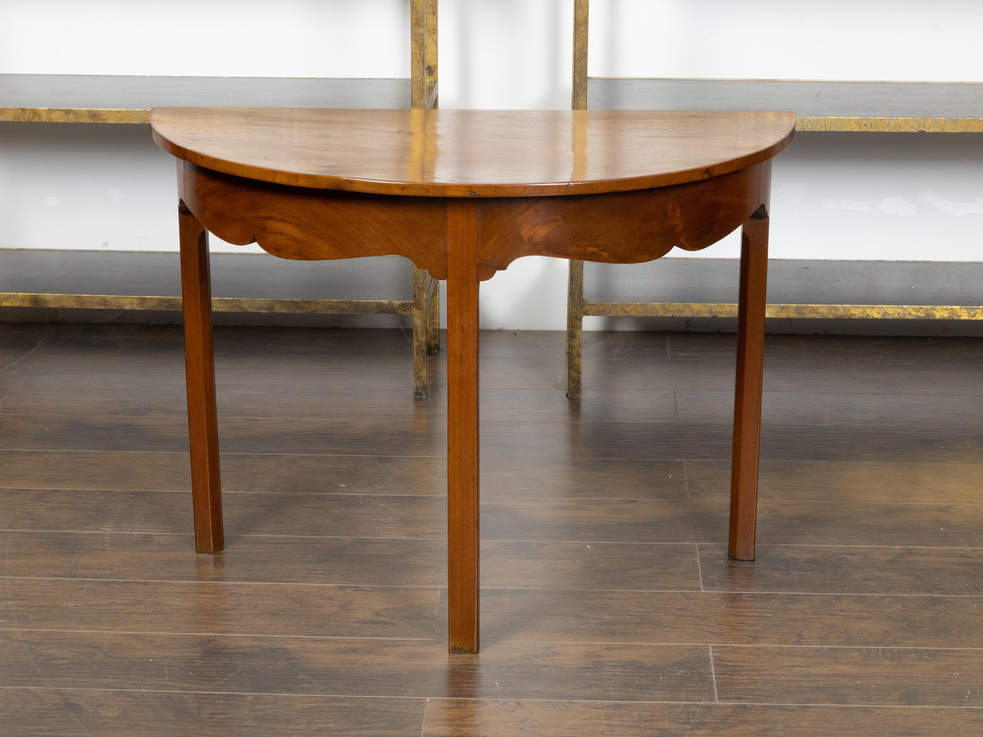 An English mahogany demi-lune side table from the 19th century, with semi-circular top, carved apron and straight legs. Created in England during the 19th century, this mahogany demi-lune side table features a semi-circular veneered top sitting