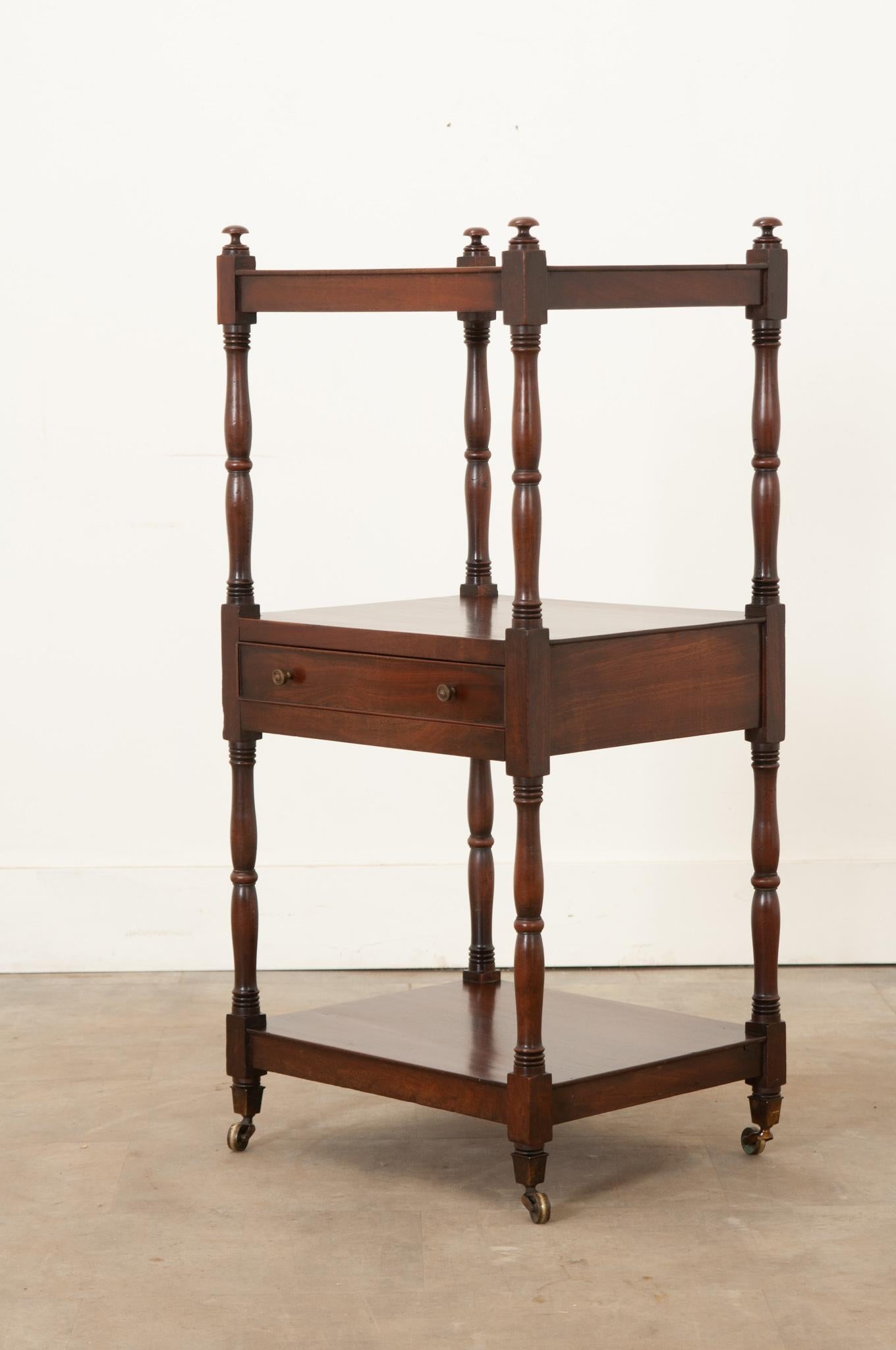 A 19th century English mahogany etagere that features 3 well-spaced shelves and elegant hand-carved spool shaped supports. The top showcases a distinctive wood grain and the piece is polished with French wax paste to revitalize its warm tone. A
