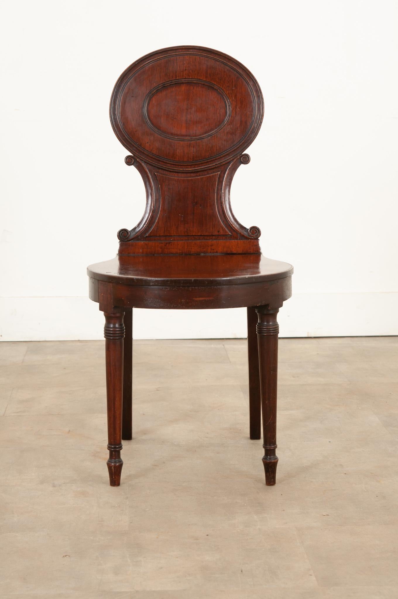 A fantastic English mahogany hall chair, made circa 1890. This handsome antique features beautifully carved details and a deep, rich coloration found within the mahogany. The front legs have been turned, while the back legs are linear, but with a