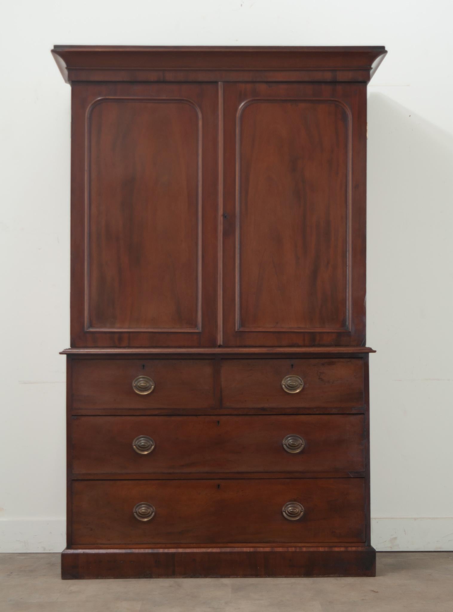 A large mahogany linen press made in England. This case piece has two paneled doors that open with a working lock and key to reveal four pull out linen press shelves at 16” deep. The bottom holds a chest of four roomy drawers, all with brass drawer
