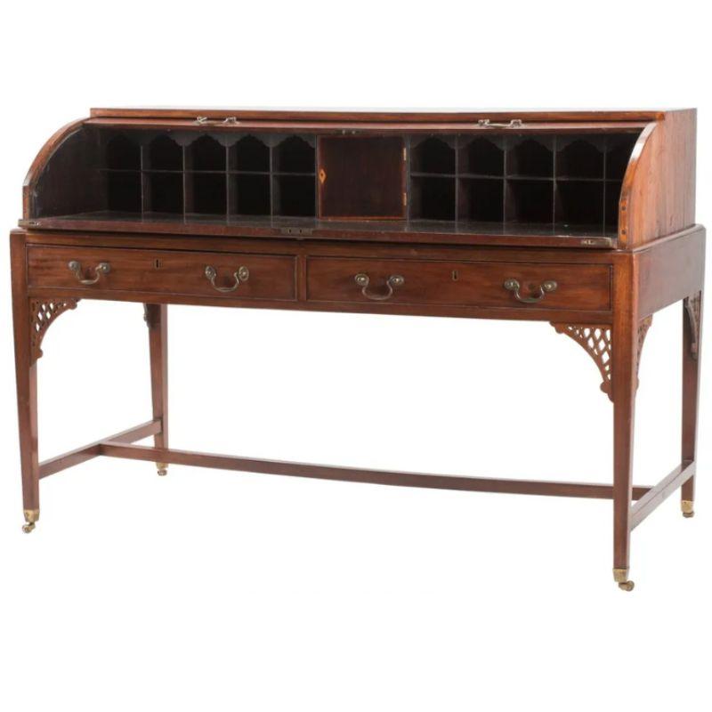 A 19th century, English mahogany roll top writing desk with two drawers and four bales in front with fretwork detail on apron at corners, and straight legs ending on casters with a single center stretcher. The tambour top opens with two bales to a