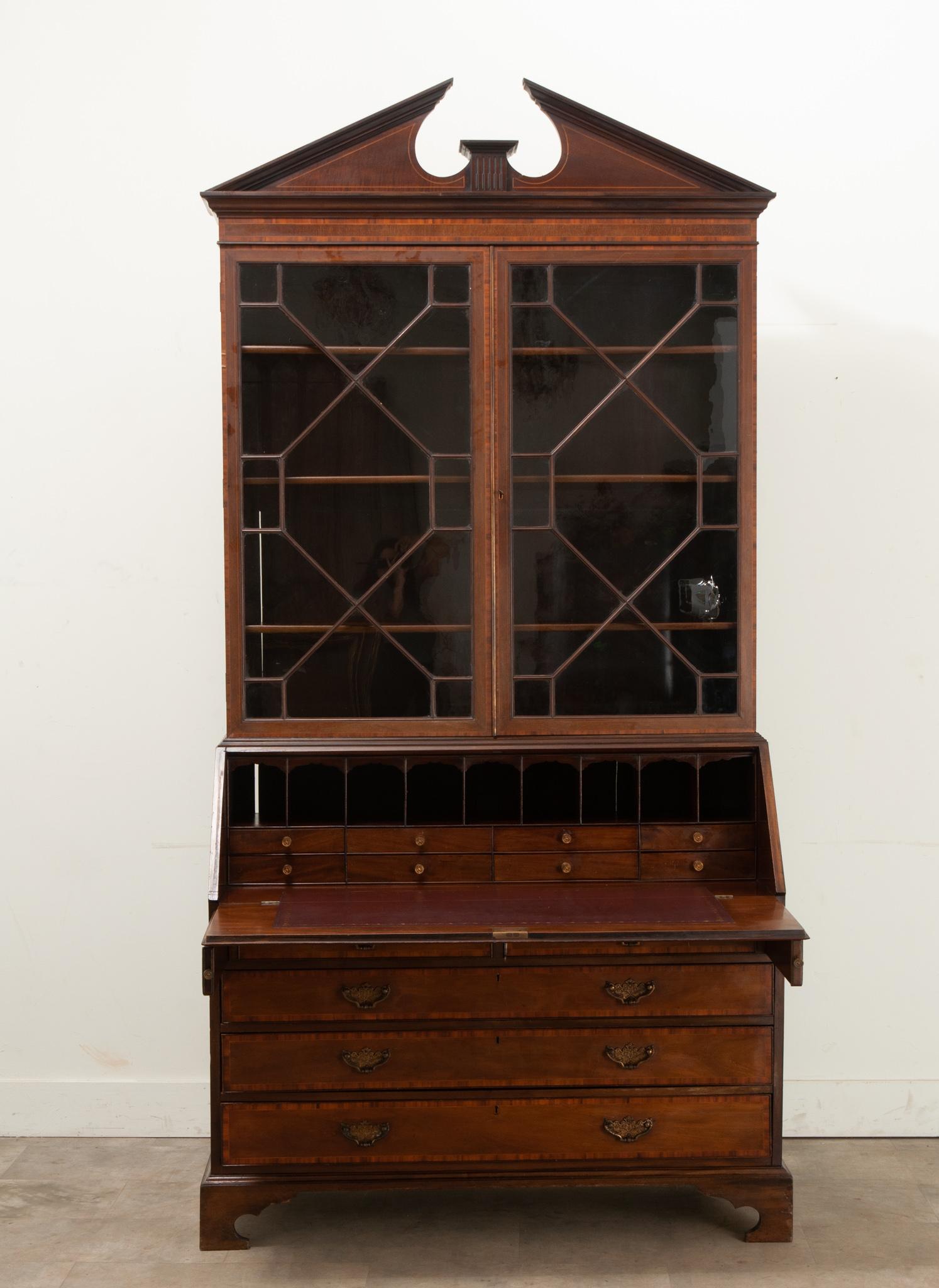 A mahogany secrétaire made in England circa 1890. This secrétaire is topped with a broken pediment design over a pair of glass front doors that open with a working lock and key. Inside are three adjustable shelves at 8” deep. A drop front desk opens