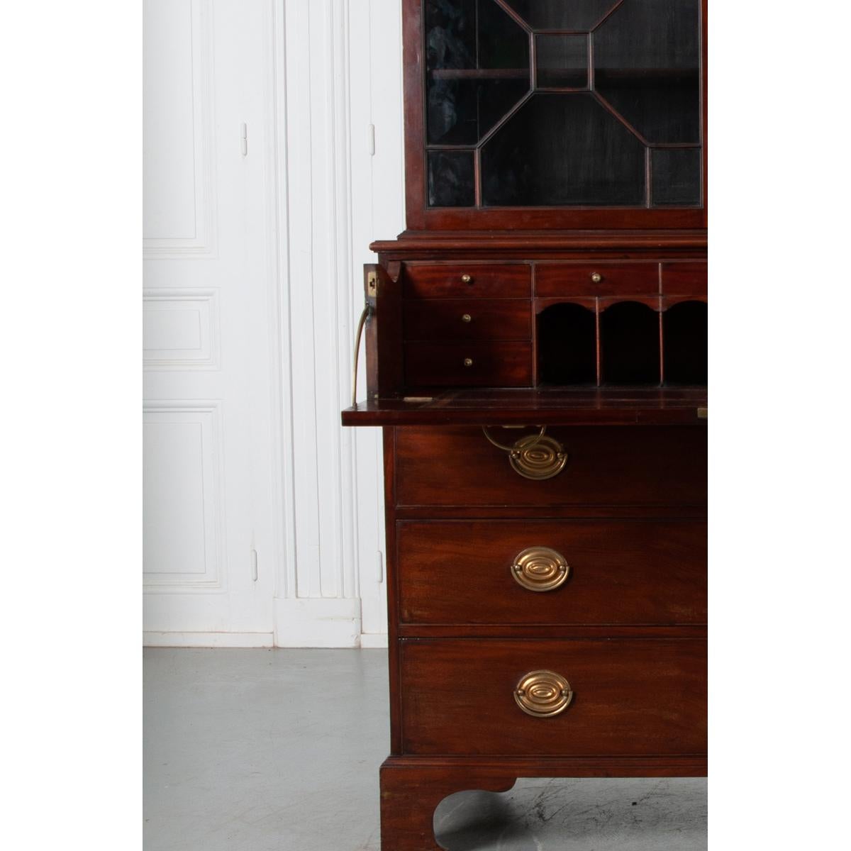 This handsome mahogany secretary from 19th century England is the perfect storage and display piece. The geometric paned glass top houses three adjustable shelves. The drop front desk hinges open to reveal a wonderfully patinated leather writing