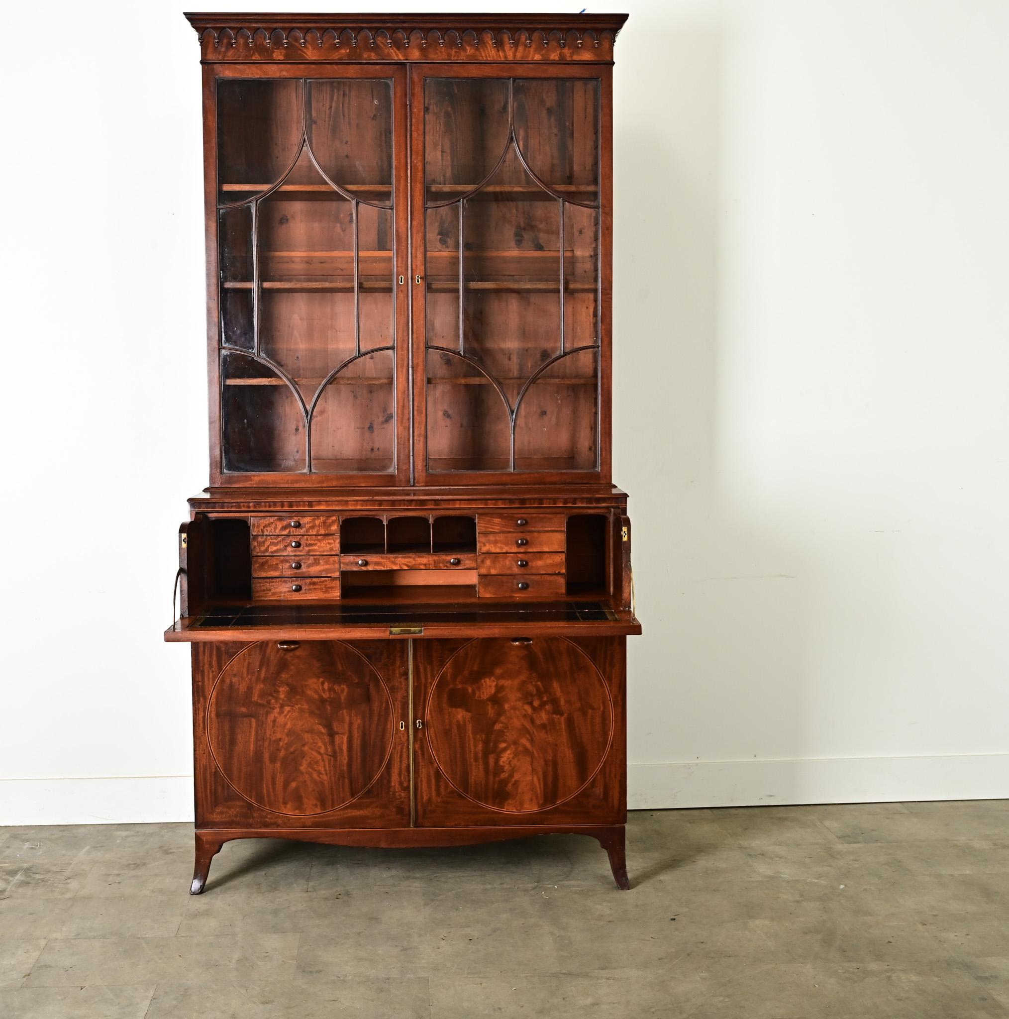 A handsome secretary from the 1800’s is made of mahogany with inlay details. The top cabinet has two glass-front bookcase doors with original glass and working lock and key, revealing three, 10 ¾” deep adjustable shelves inside. Below the pair of