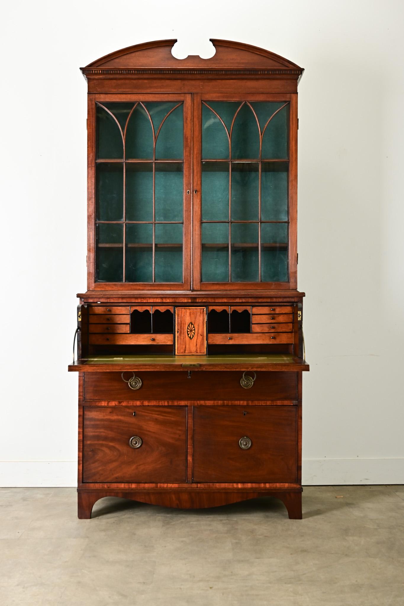 A mahogany secrétaire (secretary desk) made in England circa 1890. This secrétaire is topped with a broken pediment design over a pair of glass-front doors of original panes that open by working lock and key. Inside are two adjustable shelves at 12