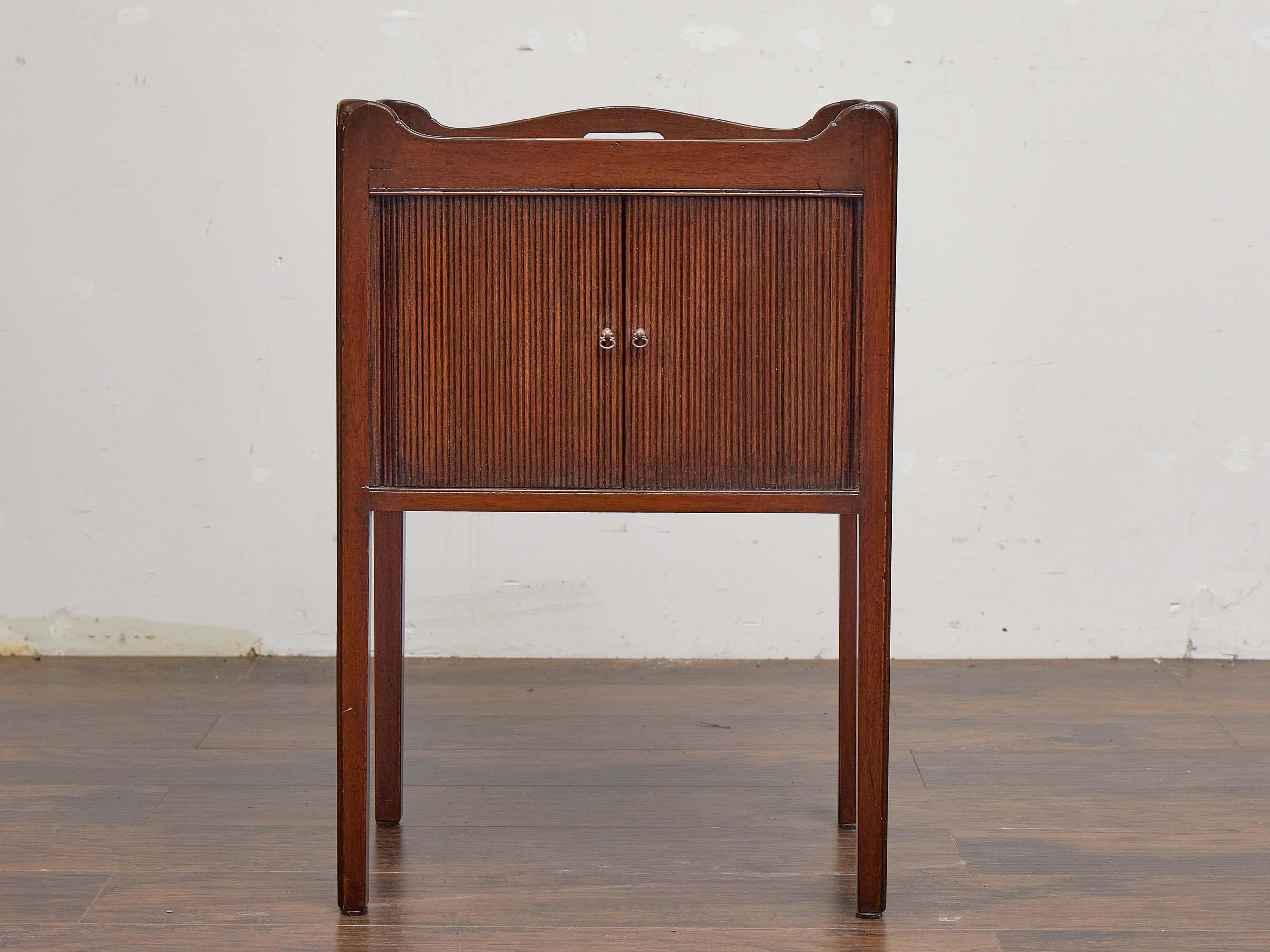 An English mahogany side cabinet dating to the 19th century, crafted with a focus on both utility and elegance. The rectangular form is topped by softly scalloped gallery edges, giving a gentle decorative profile, while shaped carrying handles are