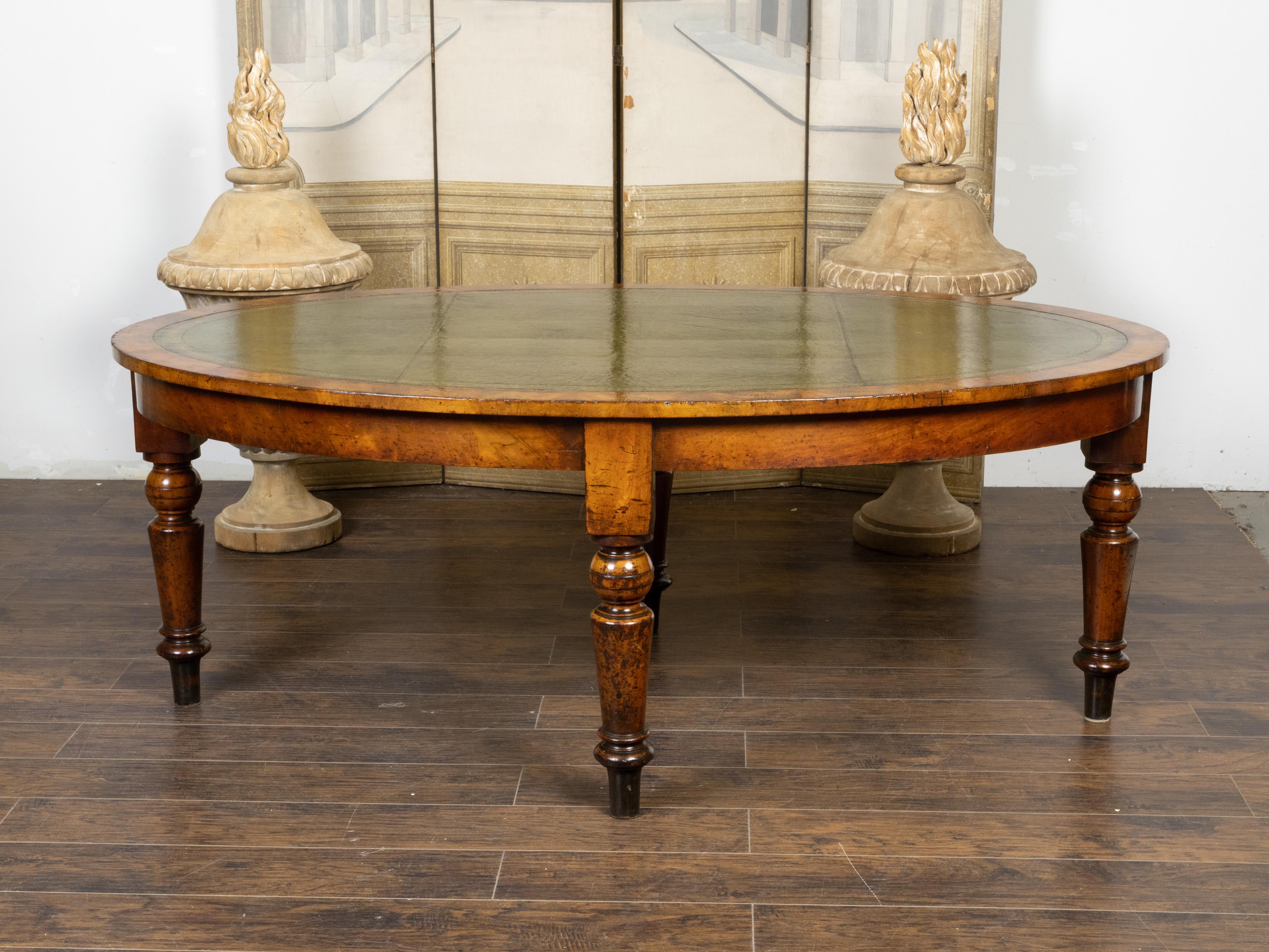 An English oval mahogany table from the 19th century, with green leather top, gilt and tooled arabesques, turned legs and nice patina. Created in England during the 19th century, this mahogany table features a green leather oval top accented with