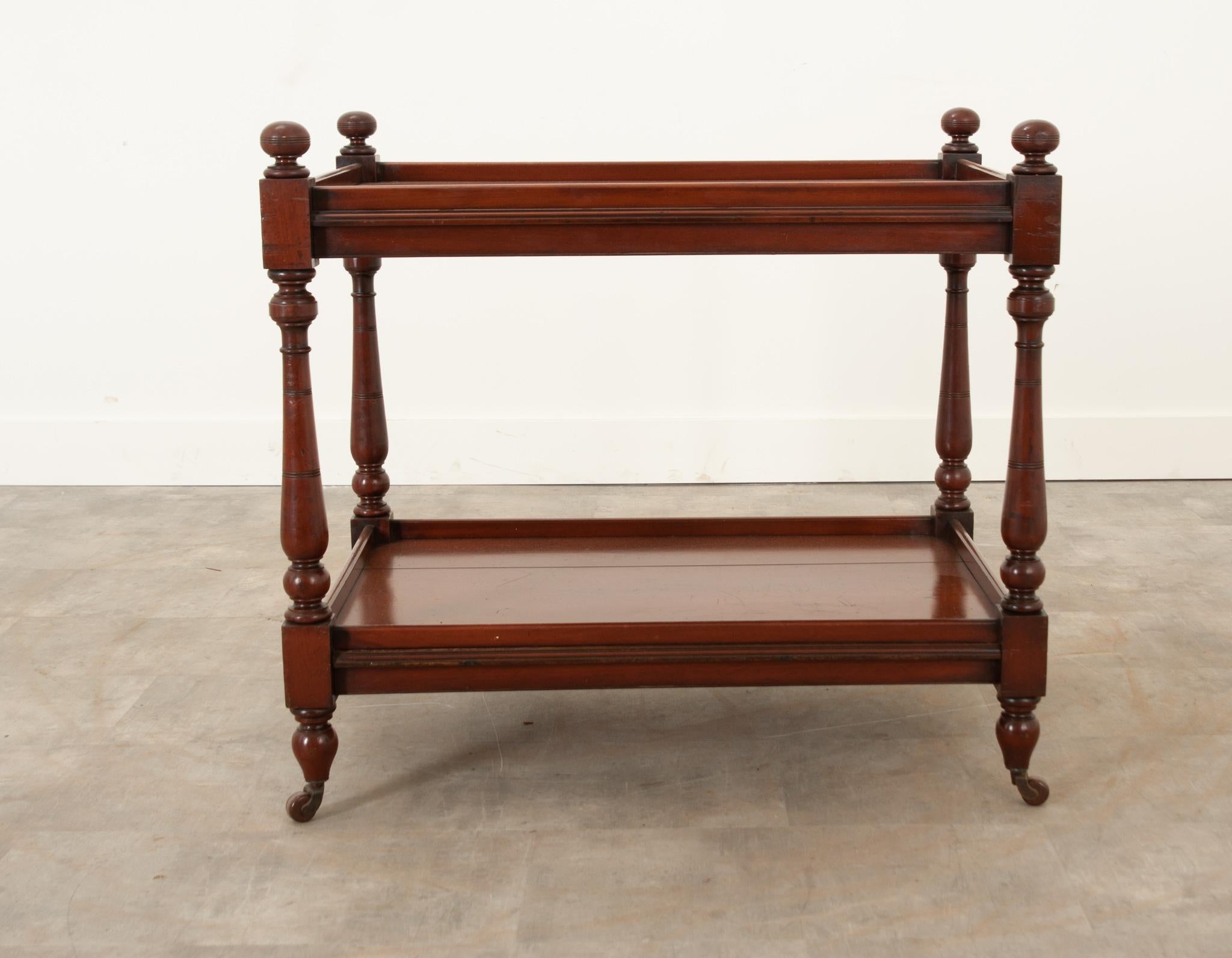 An English tea trolley crafted in the 19th century. The mahogany is stunning, with a deep, rich color and lovely patina. Two tiers are each enclosed with a molded edge. The four upright supports have been turned and styled to give this otherwise