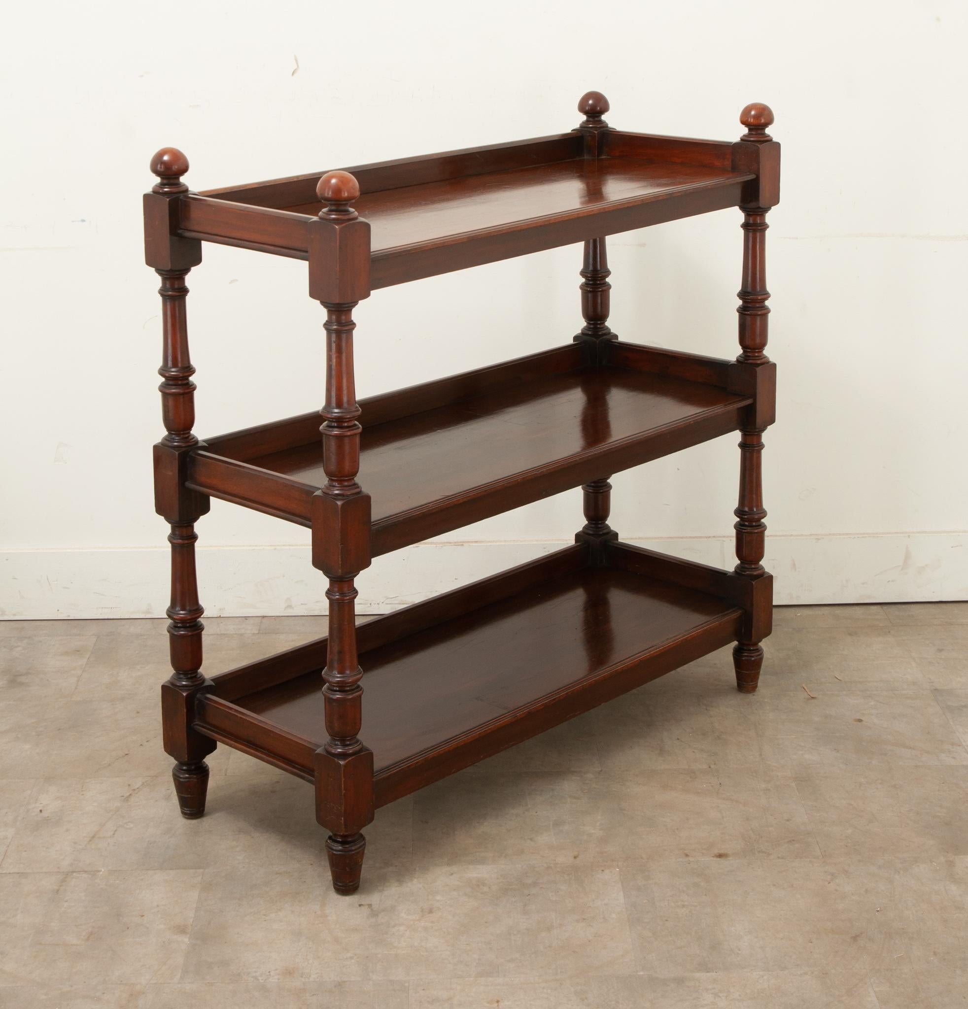 A tiered English trolley made in the 19th century. This mahogany is rich in color and has three tiered shelves. The four legs are turned and capped with turned flat finials. Cleaned and polished with a paste wax this antique is ready for your