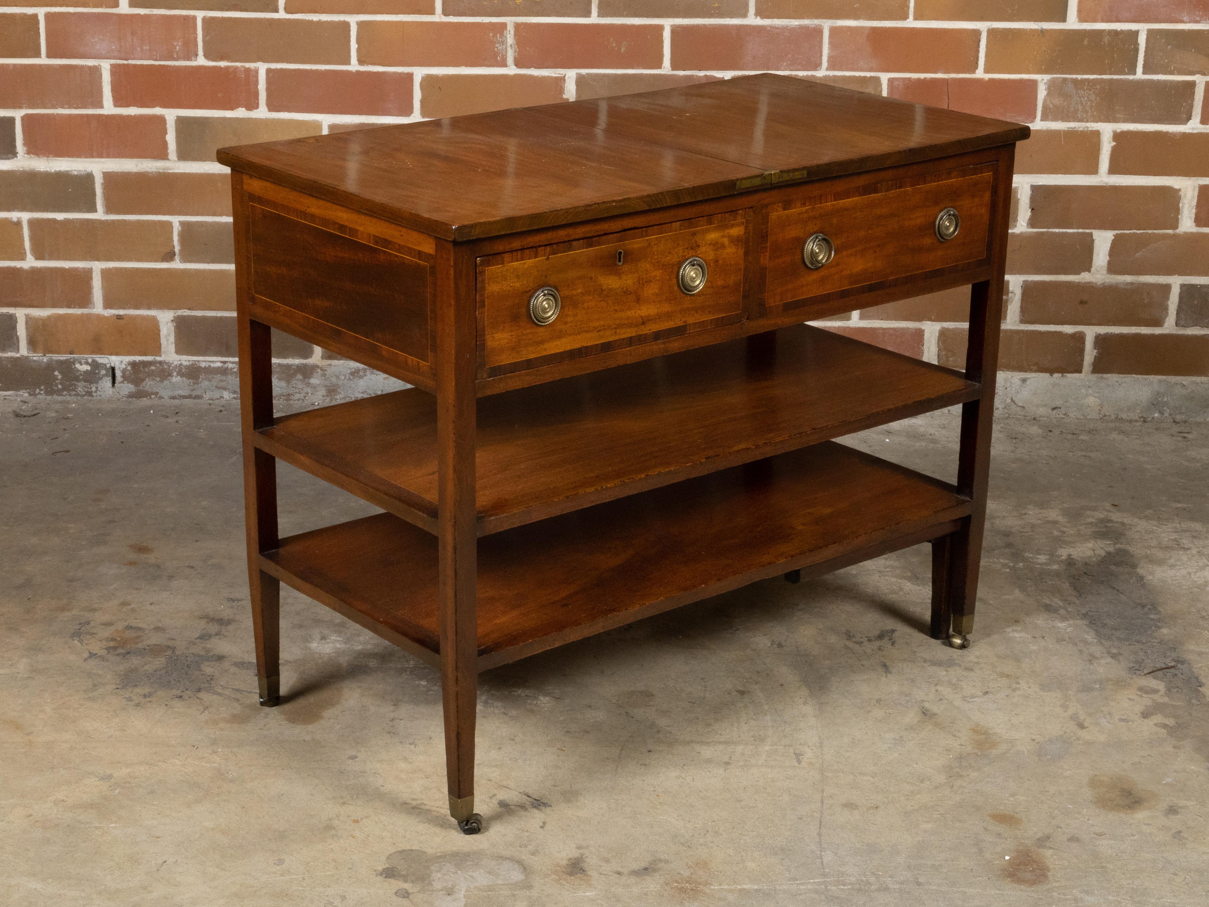 An English metamorphic table on casters from the 19th century with flip top, two drawers, cross banding, two shelves and brass hardware. Created in England during the 19th century, this table charms us with its metamorphic quality and lovely patina.