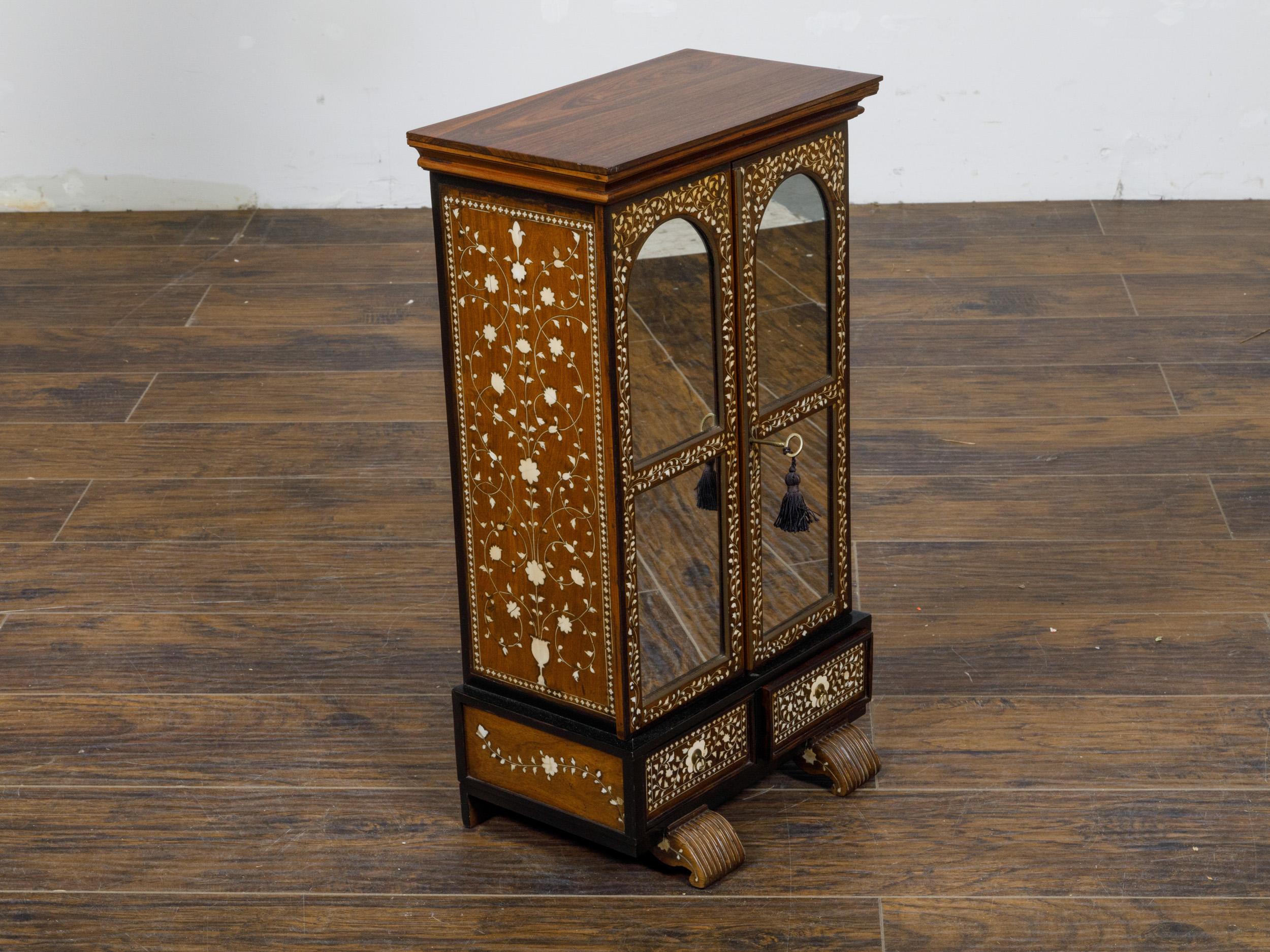 An English miniature cabinet from the 19th century with scrollwork inlay, glass doors and multiple inner drawers. This English miniature cabinet from the 19th century is an exquisite representation of Victorian craftsmanship. The cabinet features