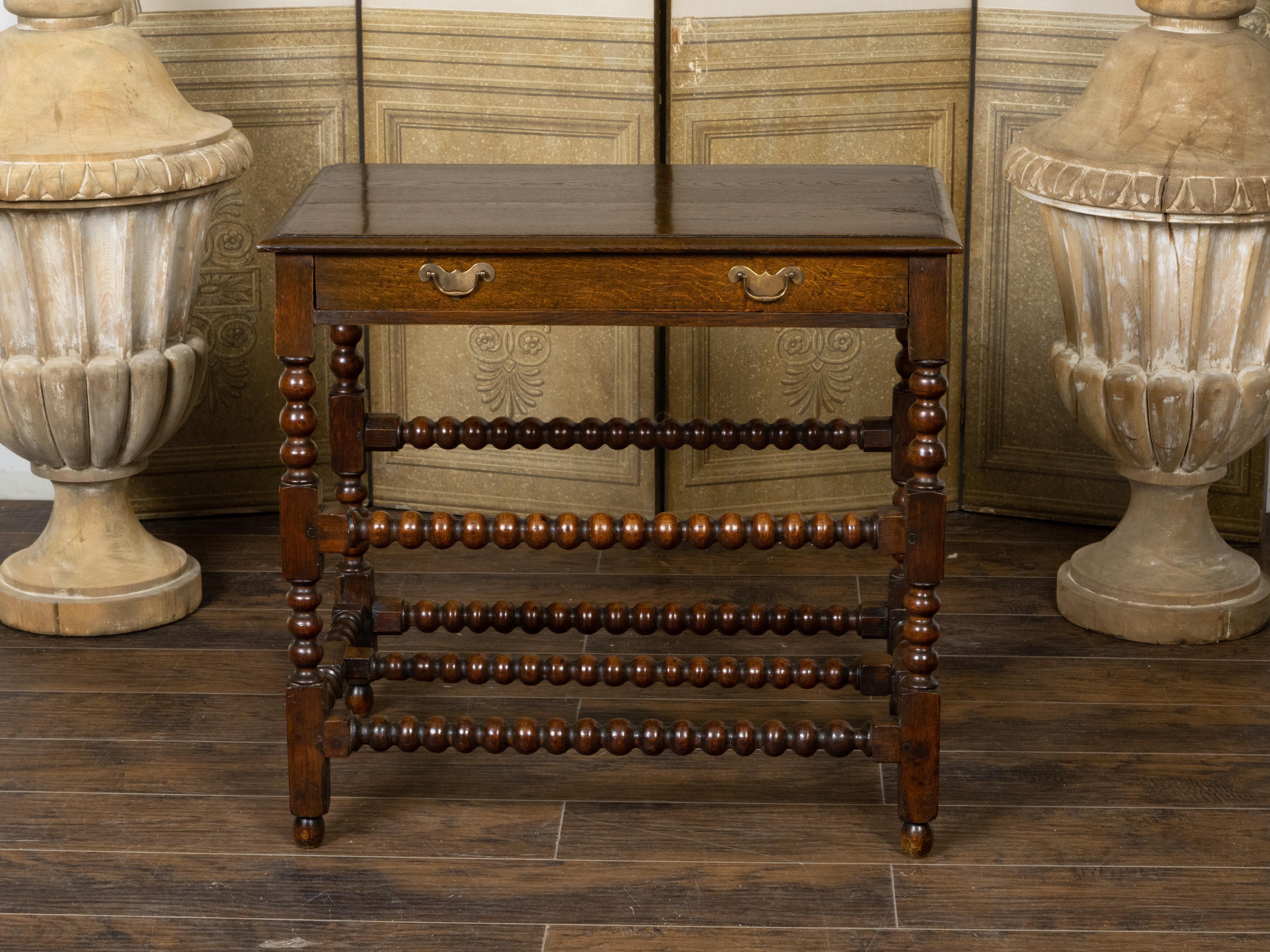 An English oak table from the 19th century, with bobbin legs, single drawer. H-Form stretcher and Chippendale style brass hardware. Created in England during the 19th century, this oak table features a rectangular top with slightly raised design and
