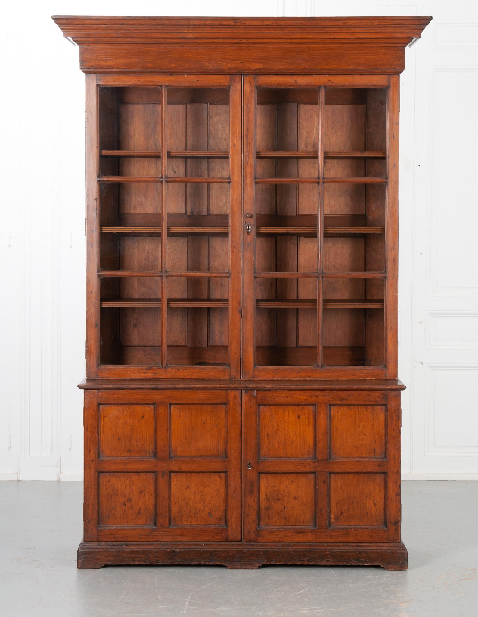 A bright four door oak bookcase with a terrific distressed quality. The large carved cornice sits heavily atop the whole of the piece. Paned original glass- front doors, unlock and unlatch open to the top storage compartment, housing three
