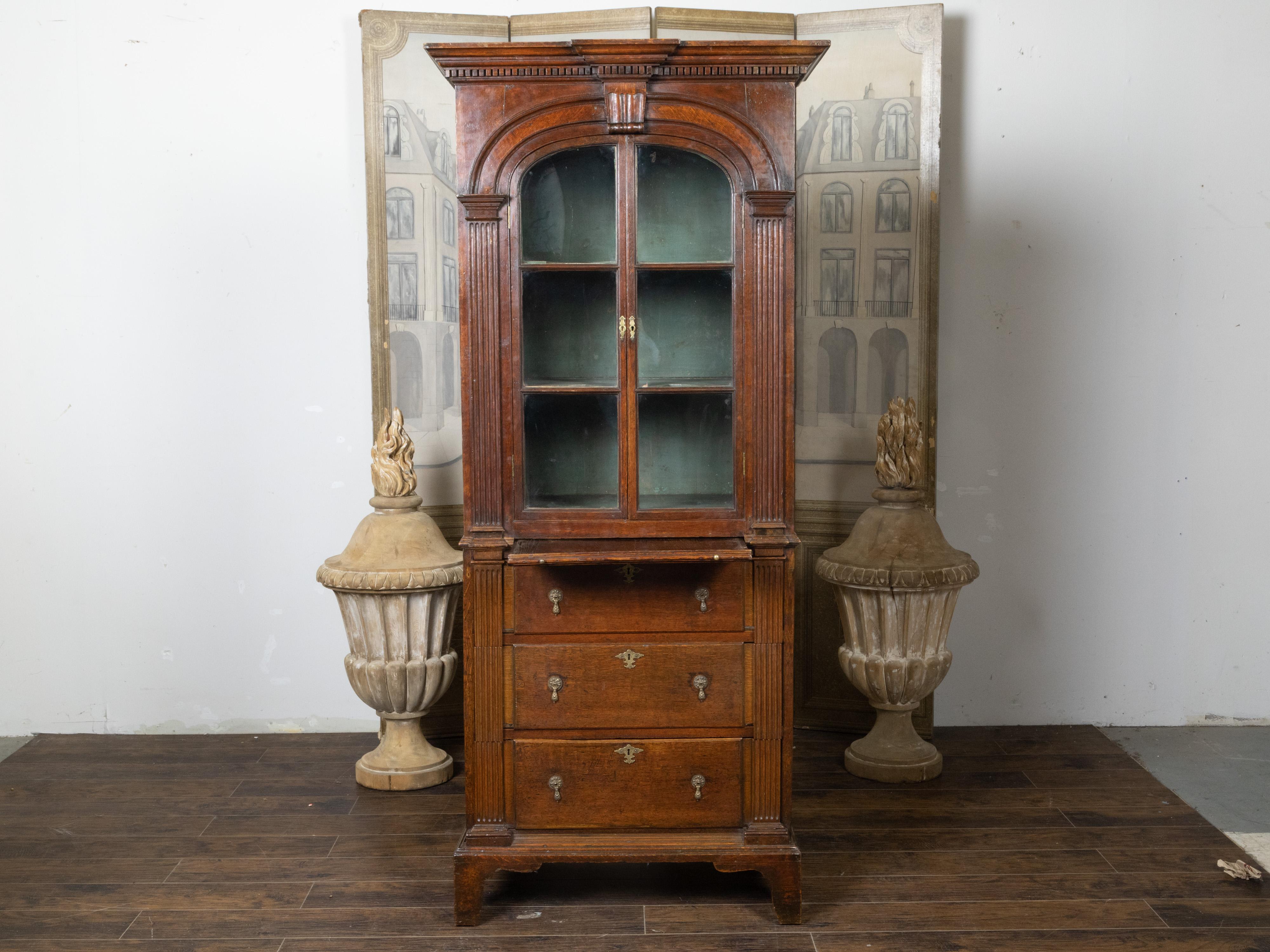An English oak bookcase from the 19th century, with carved cornice, glass doors, three drawers and pilaster motifs. Created in England during the 19th century, this oak bookcase features a molded cornice with protruding center and dentil molding,