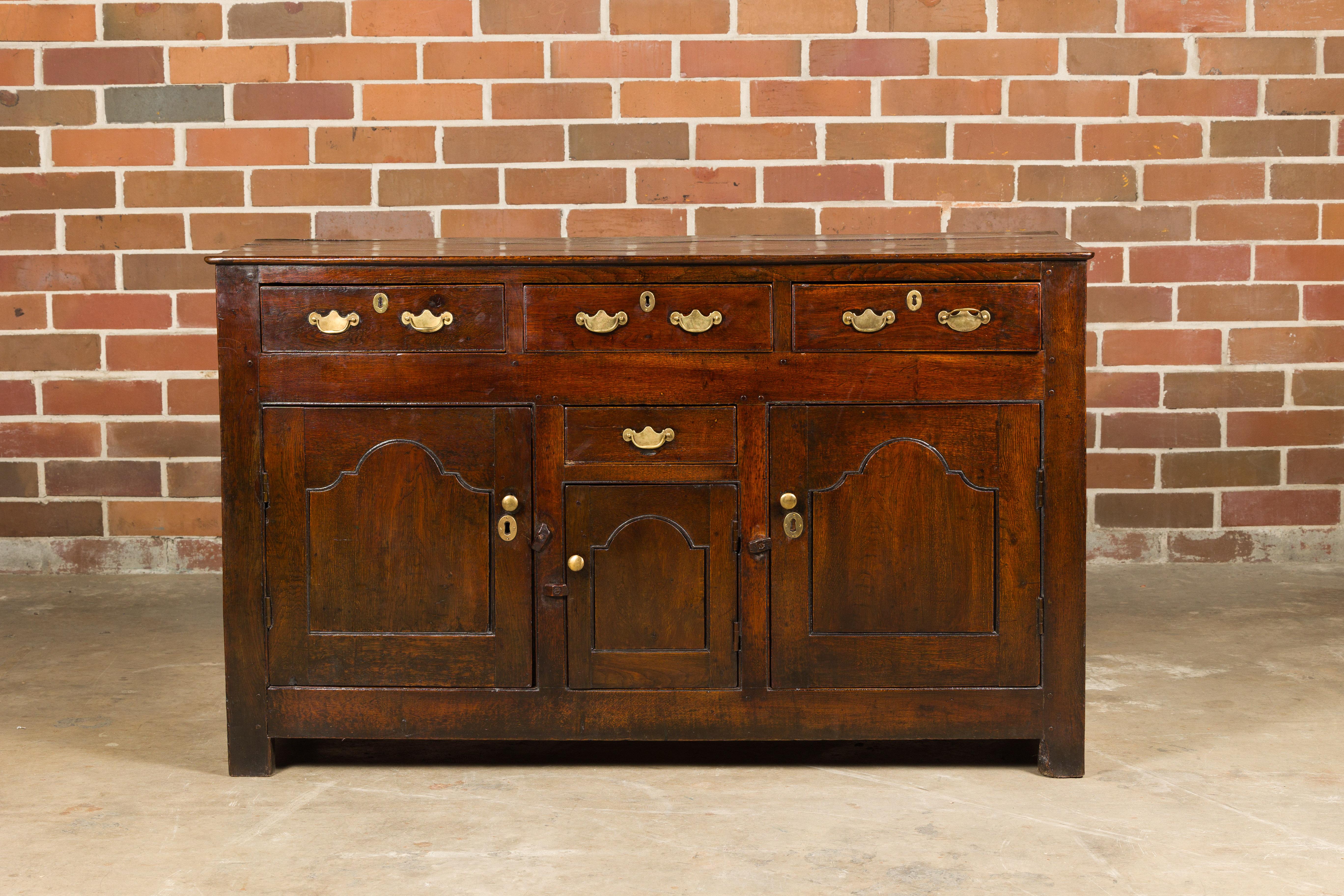 An English oak buffet from the 19th century with four drawers, three doors and brass Chippendale style hardware. Immersing us in the rich allure of the 19th century, this English oak buffet stands as a testament to classic craftsmanship. The piece