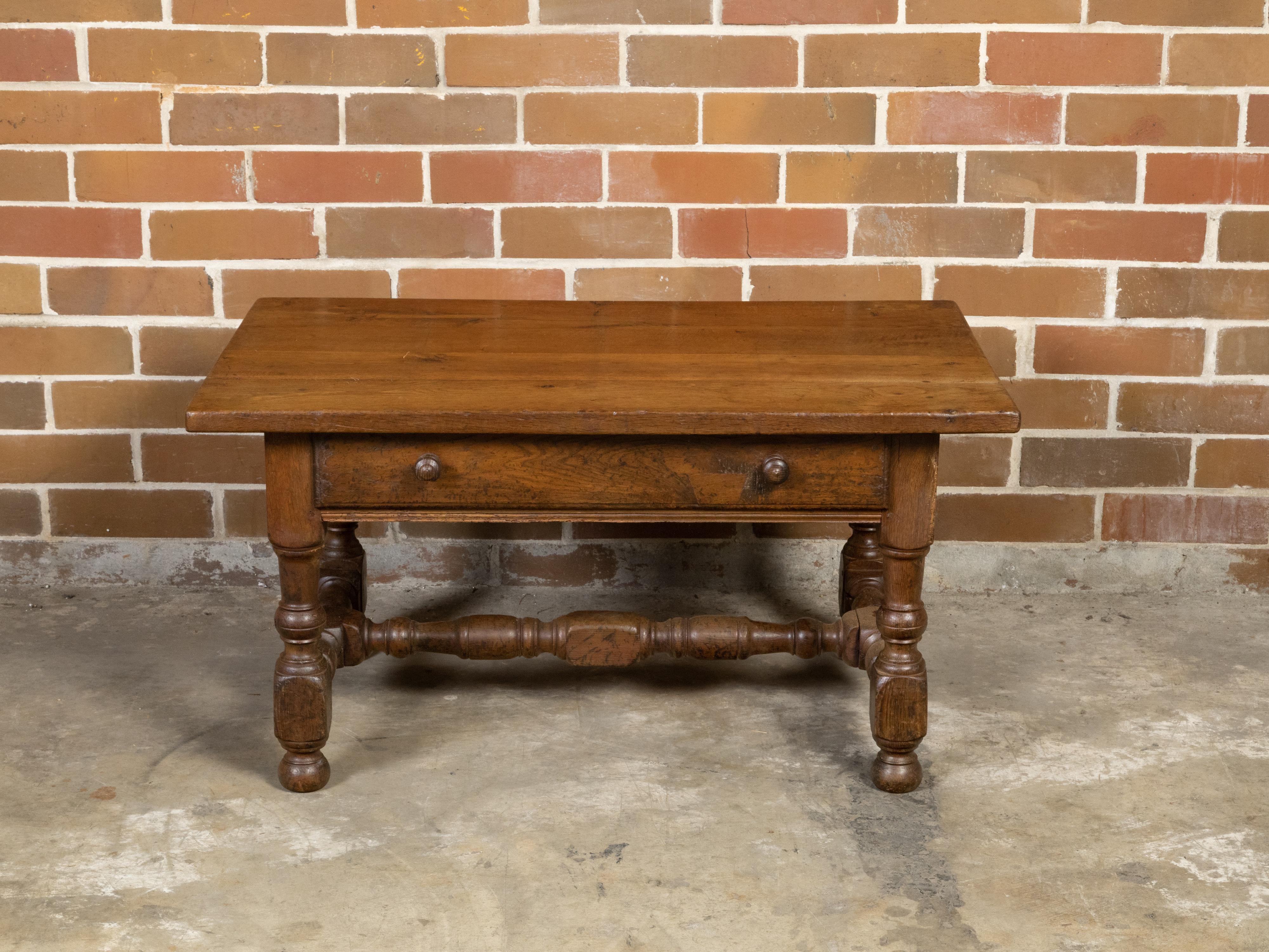 An English oak coffee table from the 19th century with single drawer, wooden pulls and turned base. Created in England during the 19th century, this oak coffee table features a rectangular planked top sitting above a single drawer, grooved for the