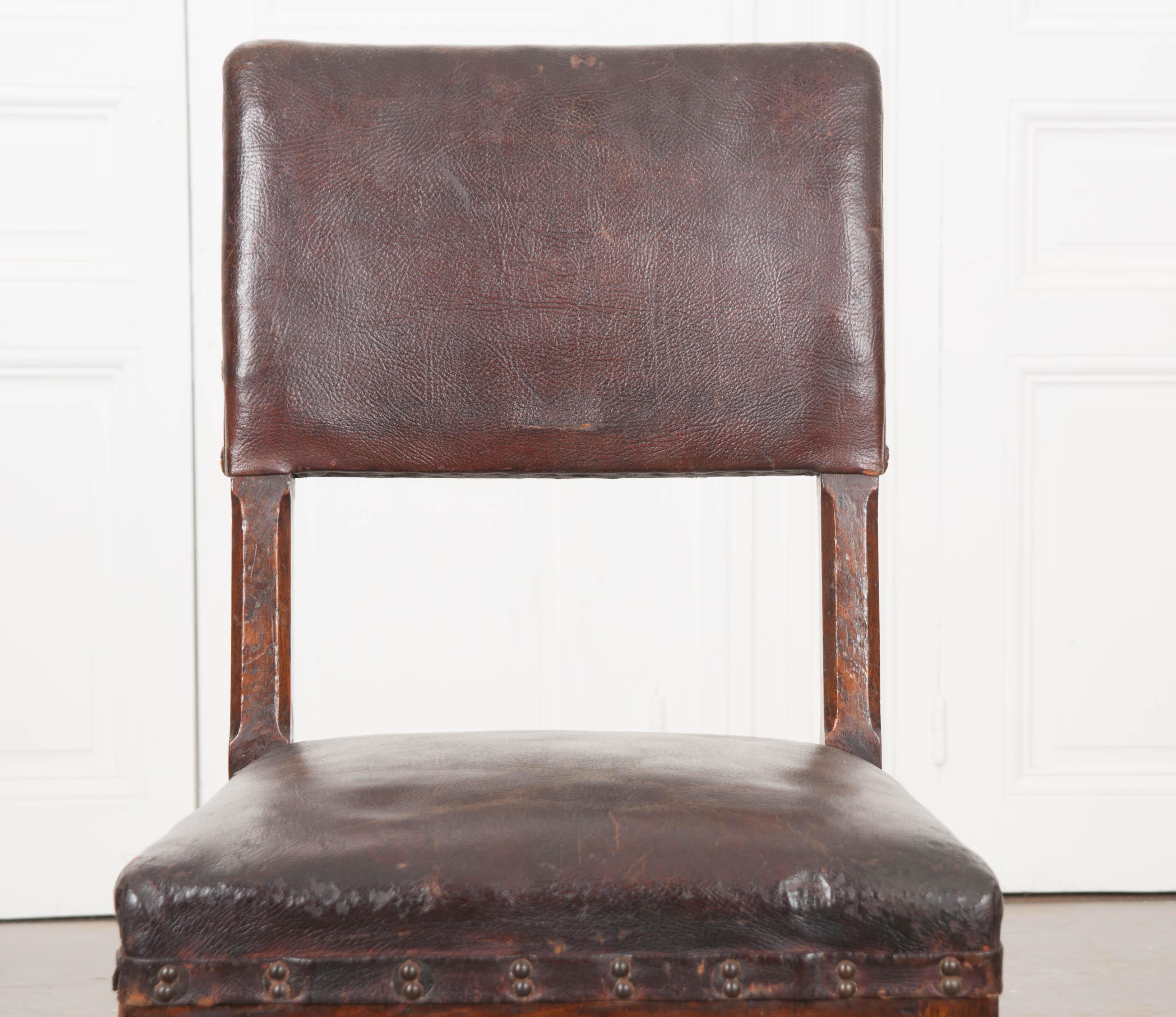 This handsome 19th century English oak desk chair, circa 1860s, features the original leather upholstery and an incredible rich patina. The padded chair back, with large decorative nail heads (several lacking), has a rear pierced handle and sits