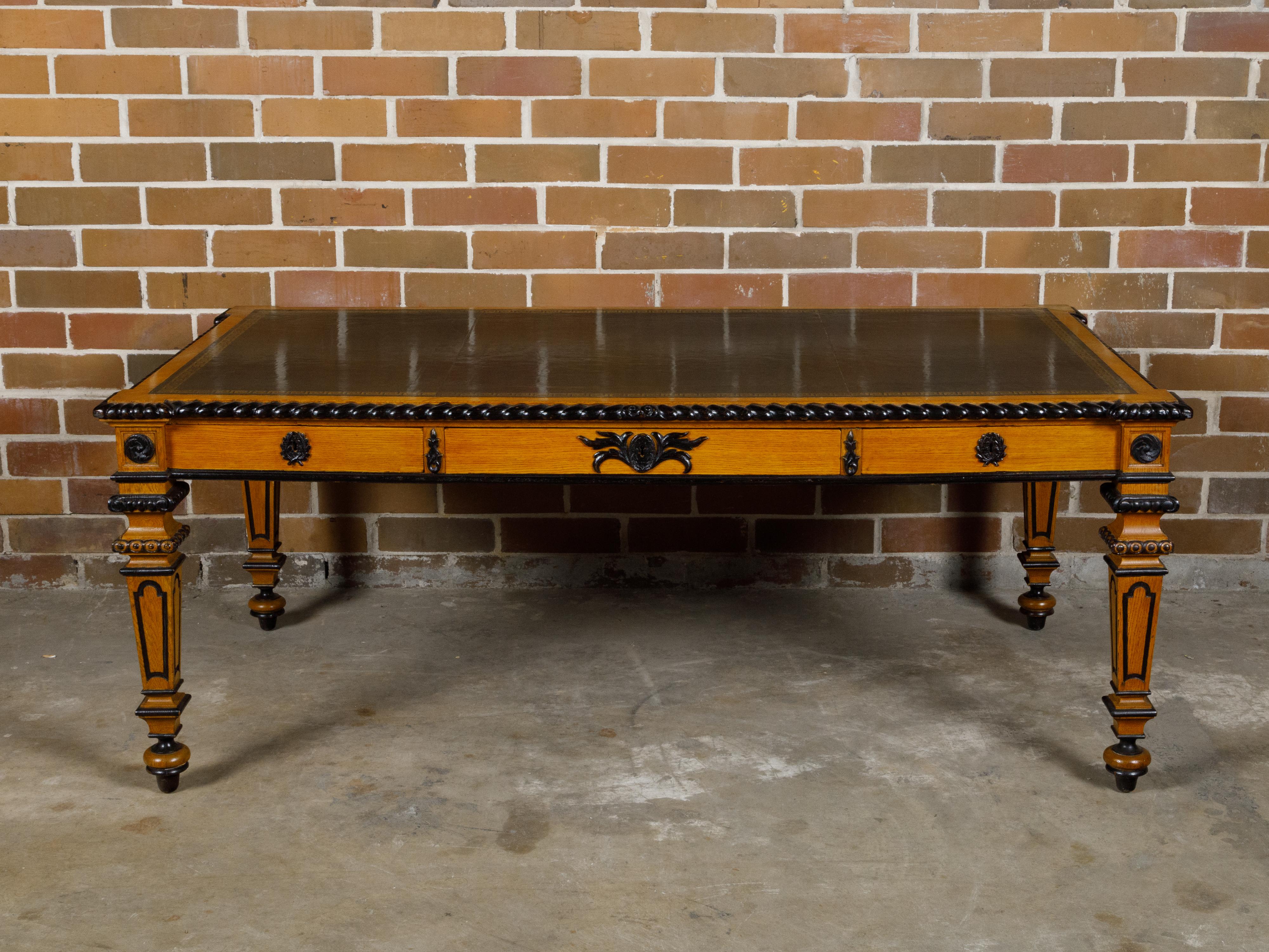 An English oak desk from the 19th century with ebonized accents, carved floral motifs and Greek Key frieze. This 19th-century English oak desk masterfully combines the warmth of oak with the sophistication of ebonized accents, creating a piece that