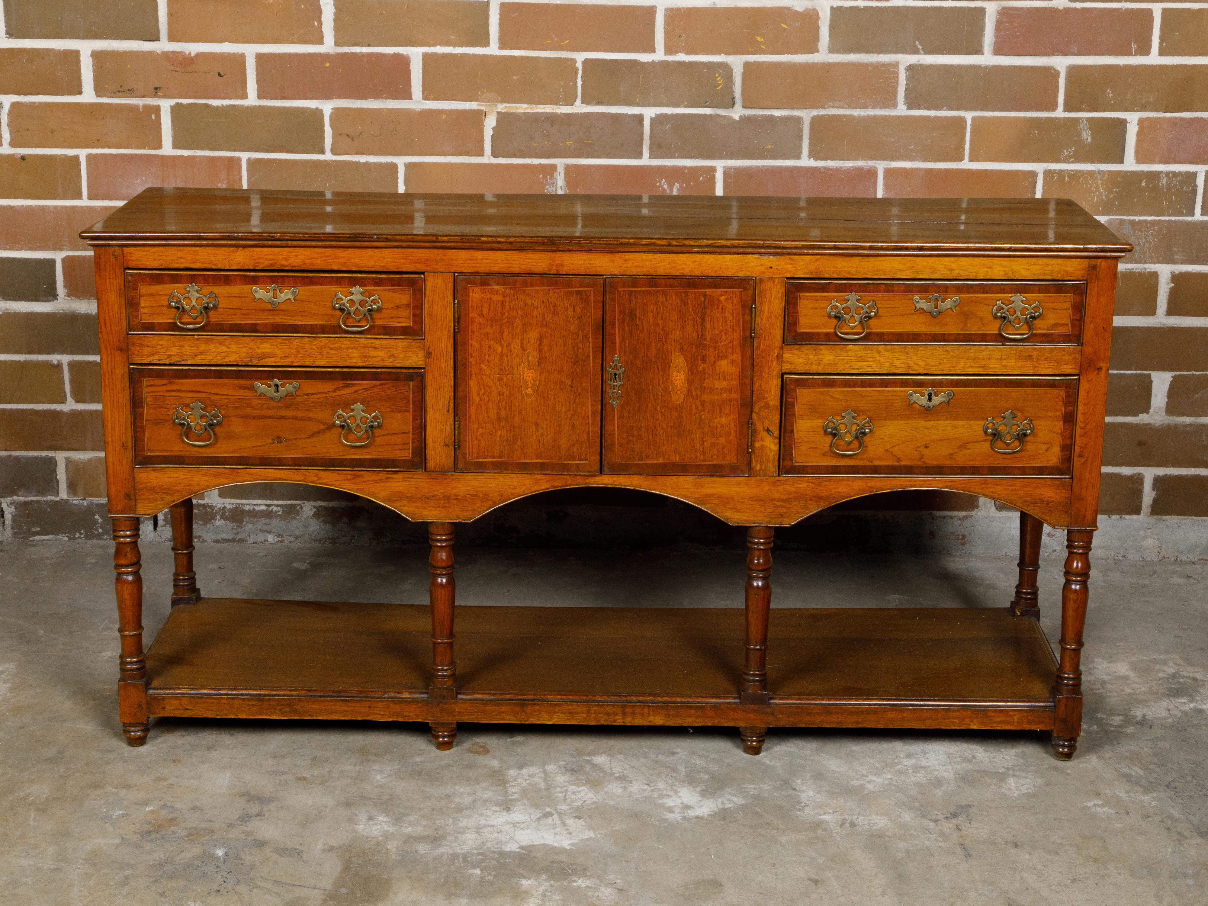 An English oak dresser base from the 19th century with marquetry, banding, doors and drawers. This 19th-century English oak dresser base is a testament to the era's exquisite craftsmanship and attention to detail. Featuring discreetly inlaid