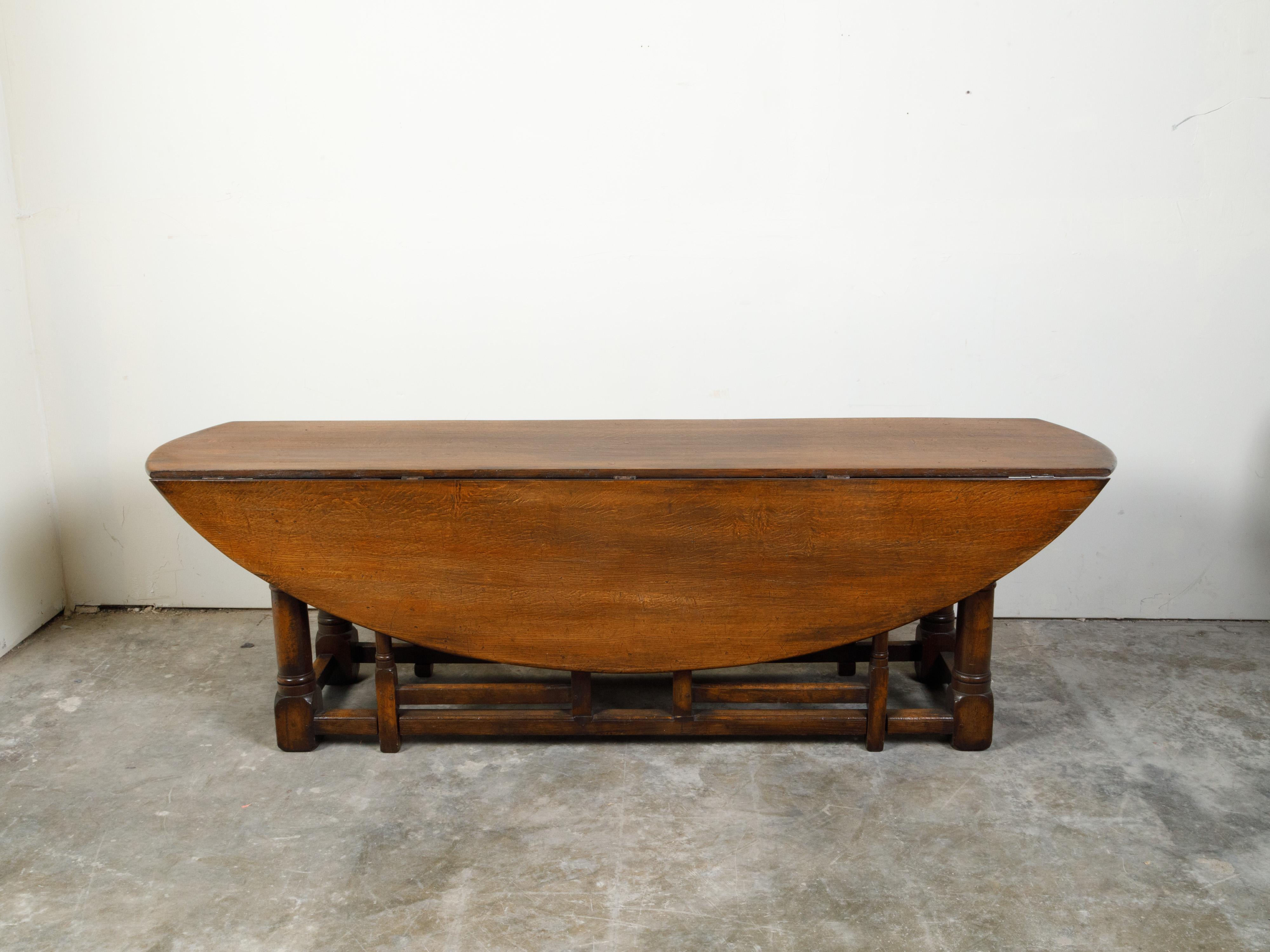 An English oak oval top drop-leaf table from the 19th century with gateleg base. Created in England during the 19th century, this oak table features an oval top made of two drop leaves. The depth of the table when the leaves are down is 24