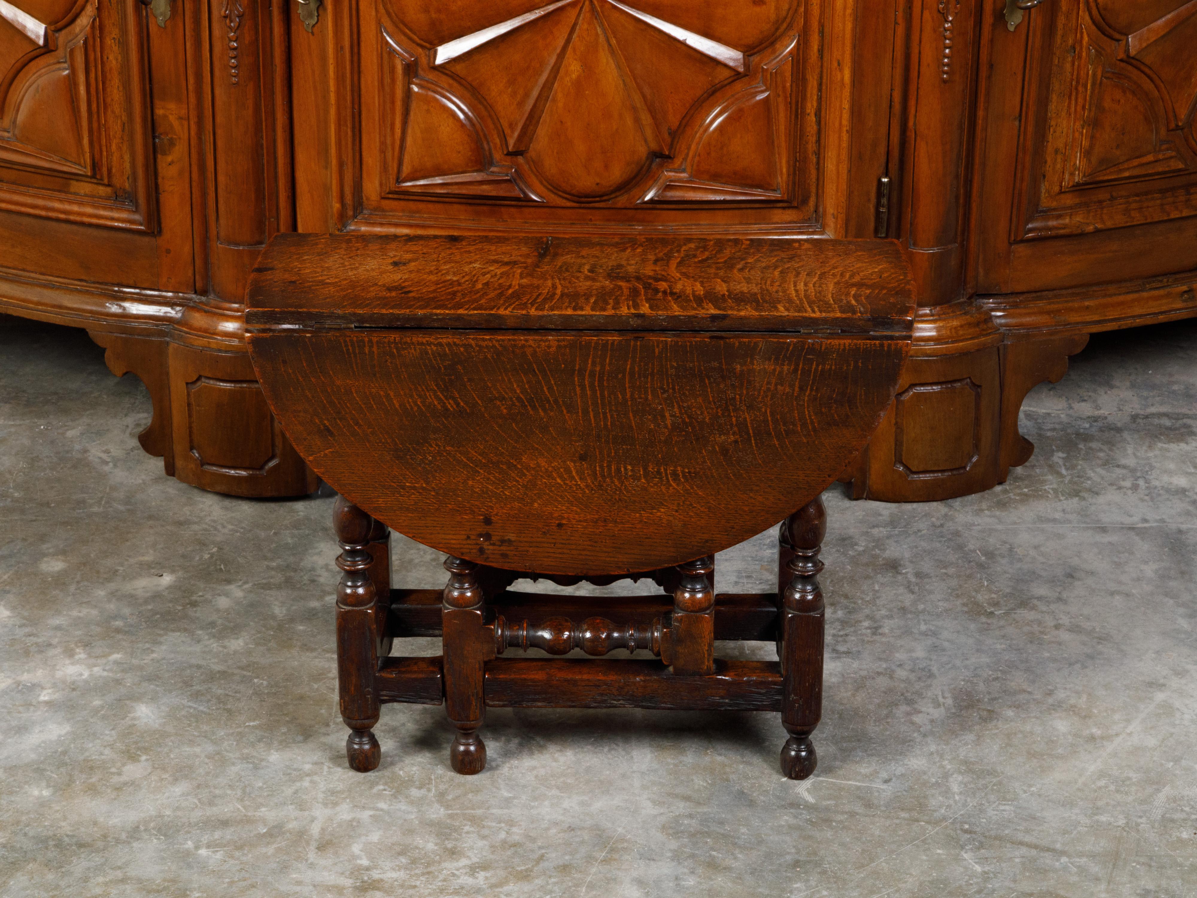 An English oak drop-leaf side table from the 19th century, with turned gateleg base. Created in England during the 19th century, this small side table features an oval top with two drop leaves (measuring 27