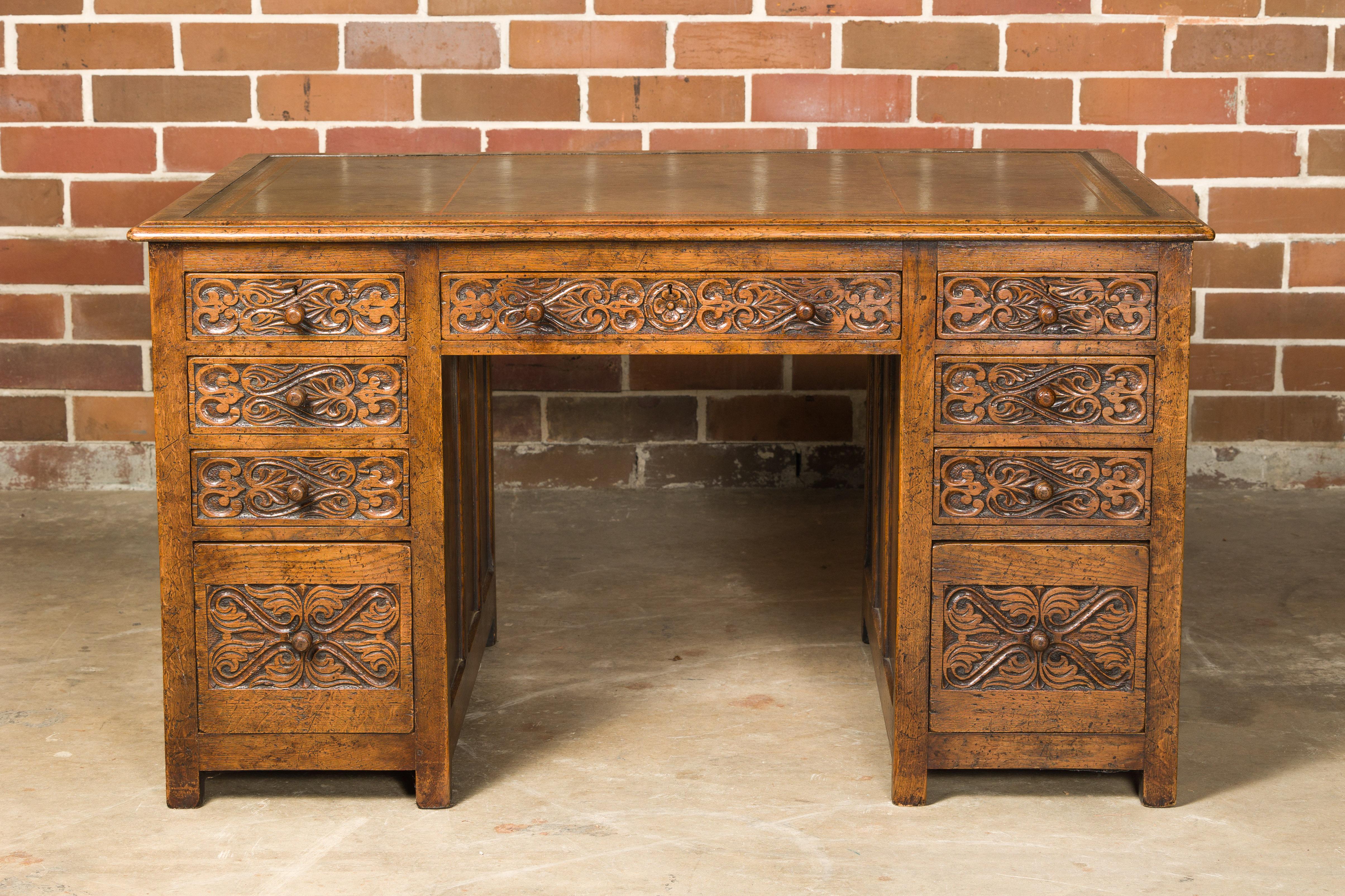 An English oak office kneehole desk from the 19th century, with green leather top, nine drawers and carved foliage décor. Enrich your home office with the enduring elegance of this English oak office kneehole desk from the 19th century. Its grand